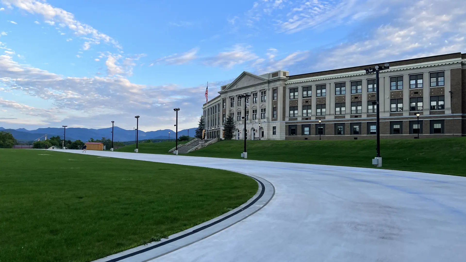 A stone high school overlooks a smooth skating track on a summer day.