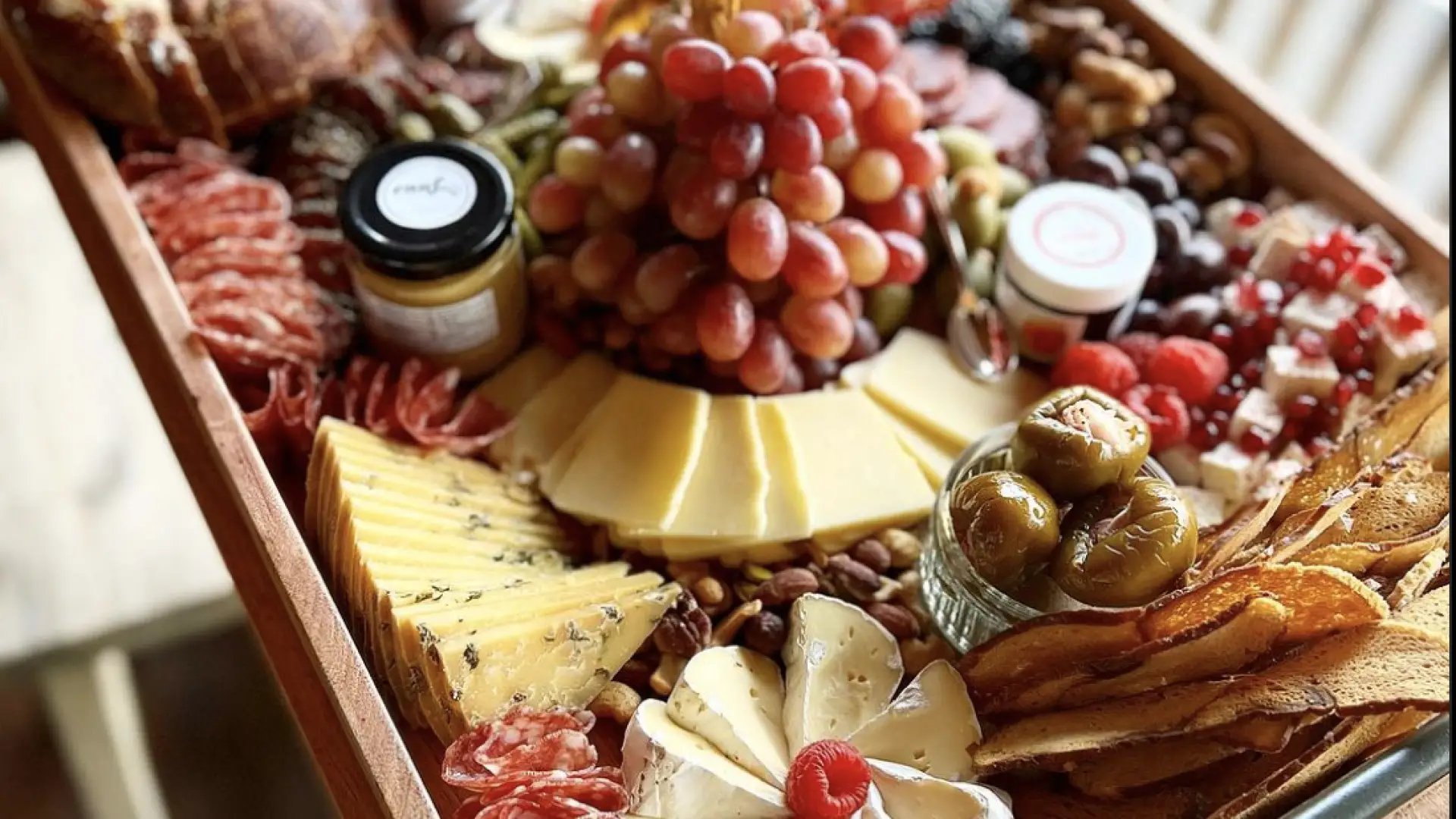 A charcuterie board with an assortment of meats, cheeses, peppers, grapes, mustard, bagel chips and more
