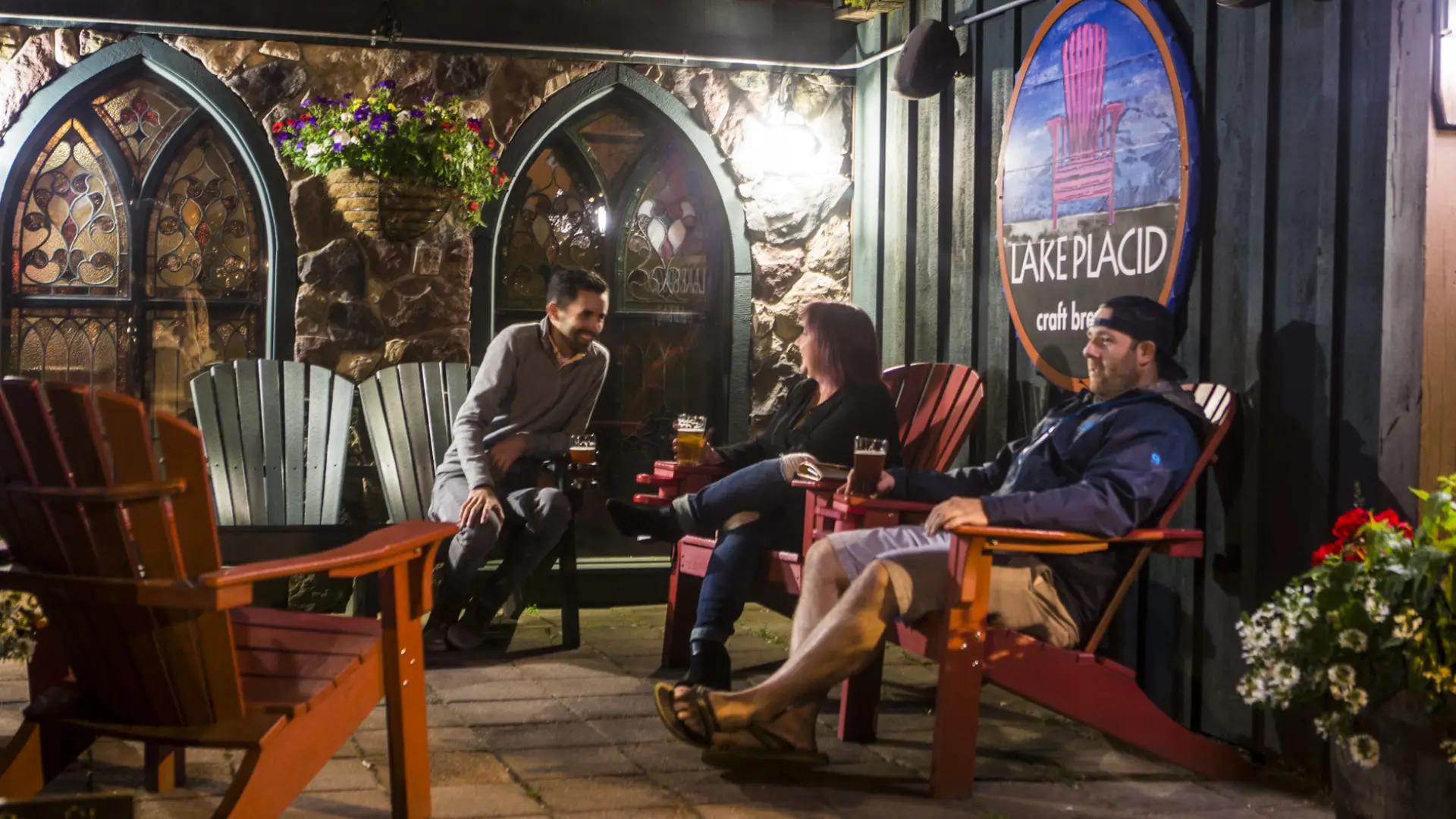 Three people socialize in Adirondack chairs at the Lake Placid Pub & Brewery.