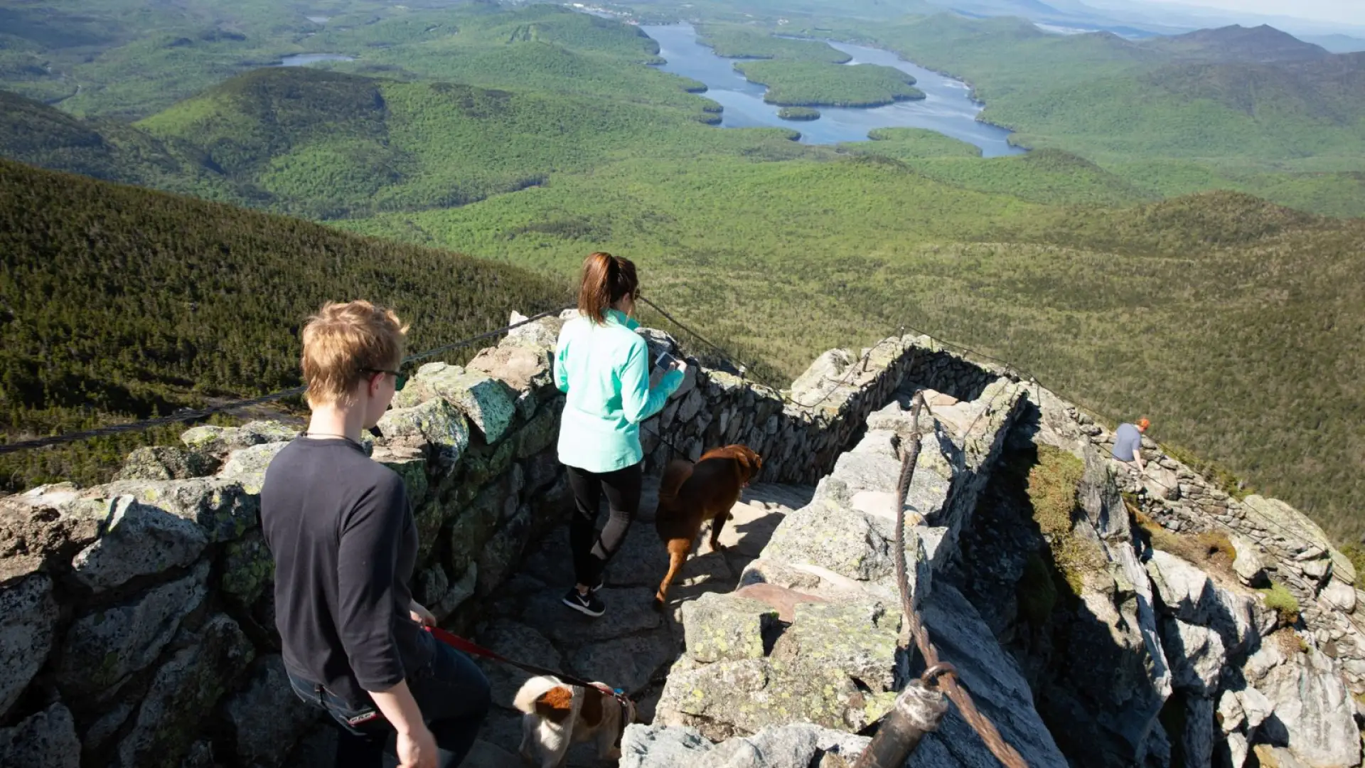 Two women walking down the stairs from the Whiteface Mountain weather station with mountains in the background.