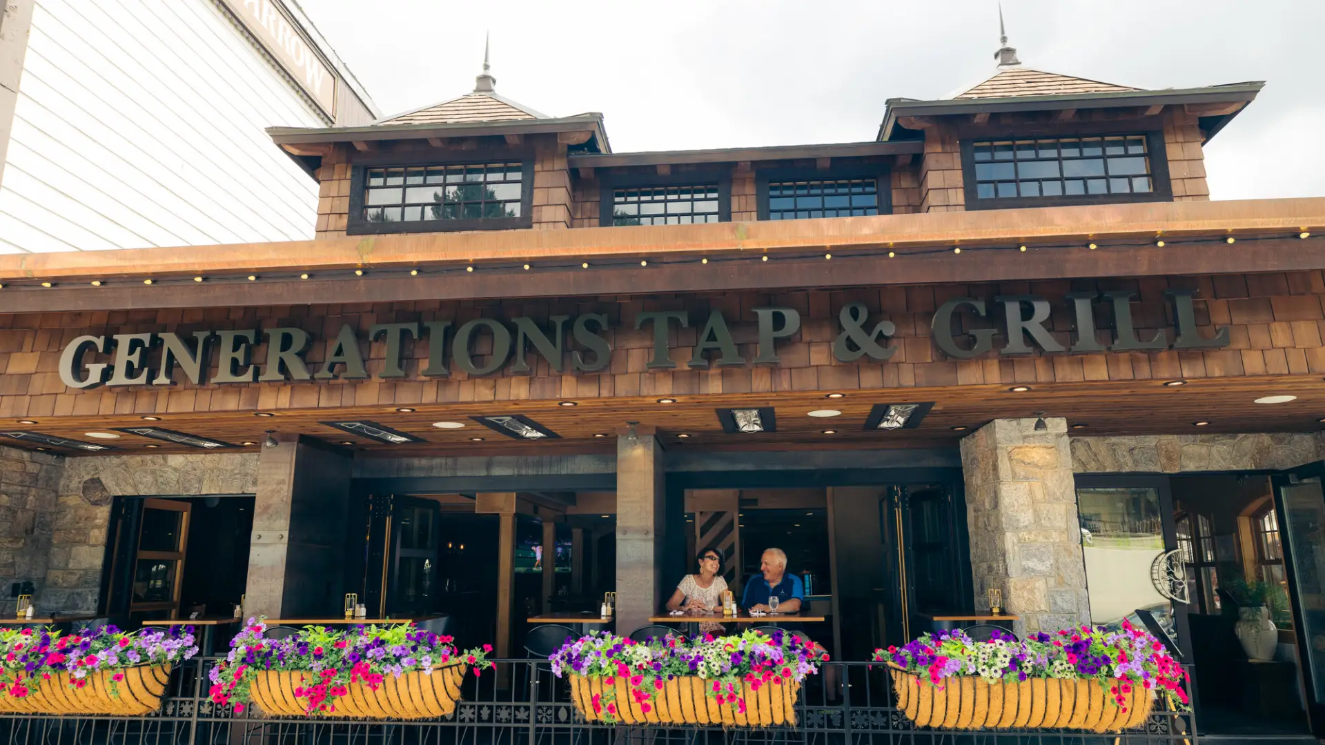 Senior couple sits at table on outdoor deck of restaurant with colorful flower boxes in front of them