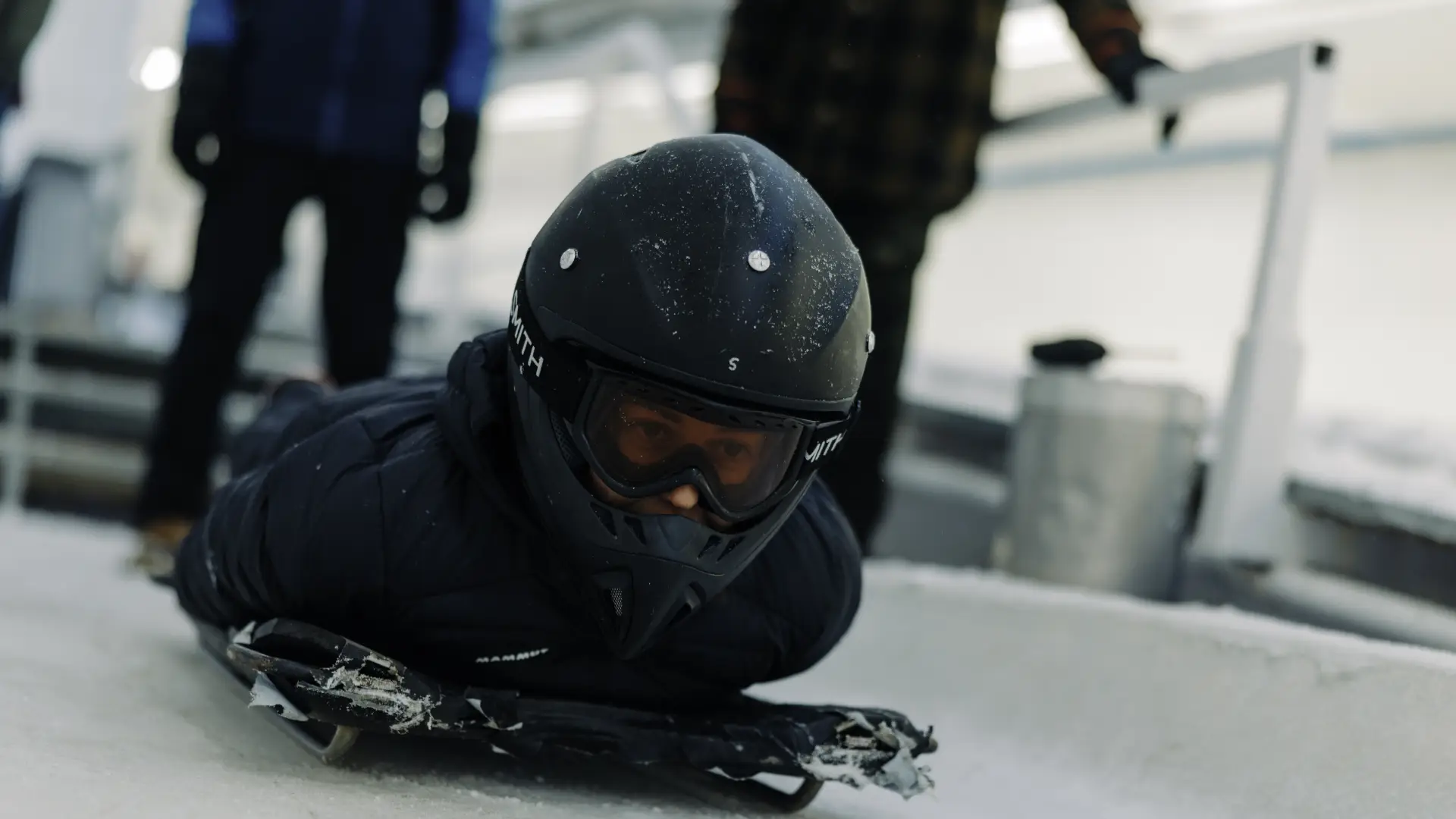 Person in helmet lays on skeleton sled on ice track