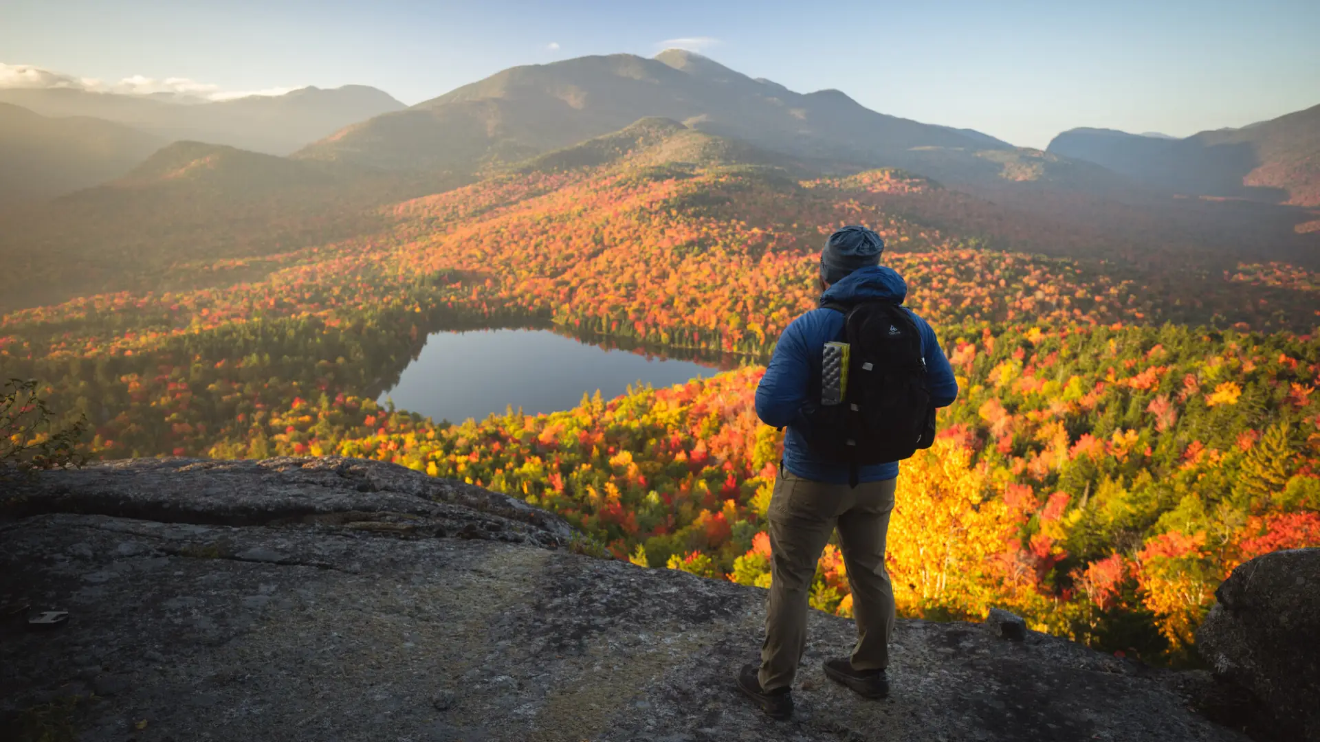 A man stands on top of a fall mountain. 