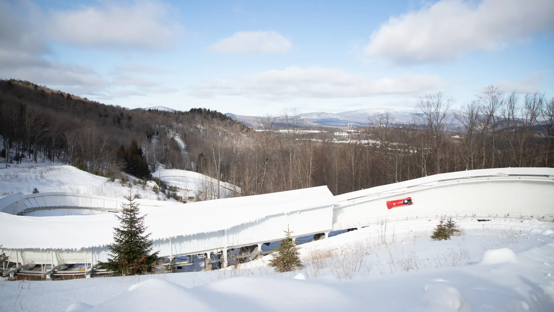 Red bobsled slides down track with mountains in background
