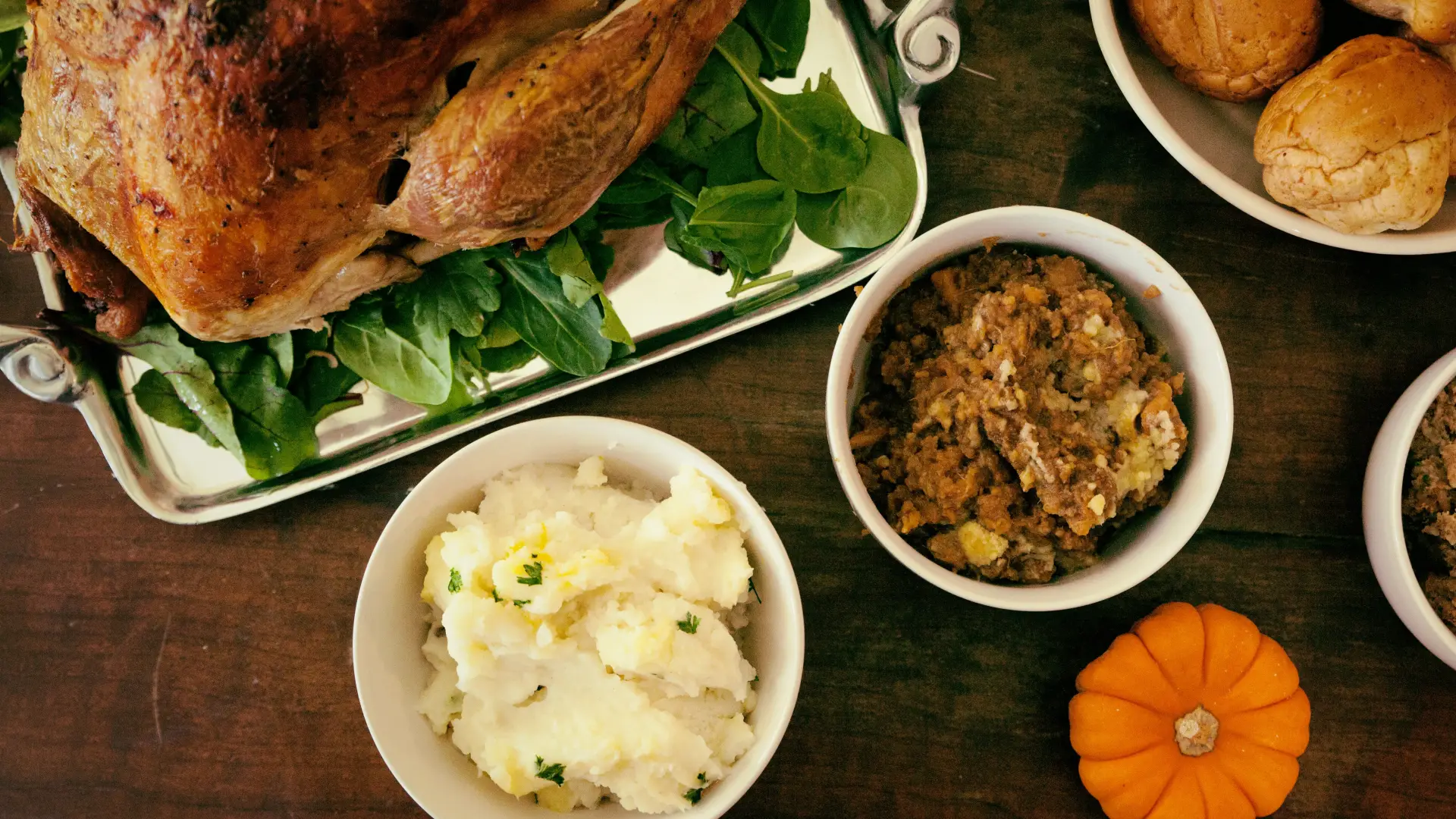 Stock image of a turkey on a platter and bowls of Thanksgiving sides on a wooden table