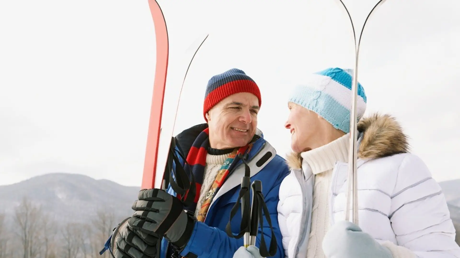 A man and woman  holding skis smile at eachother