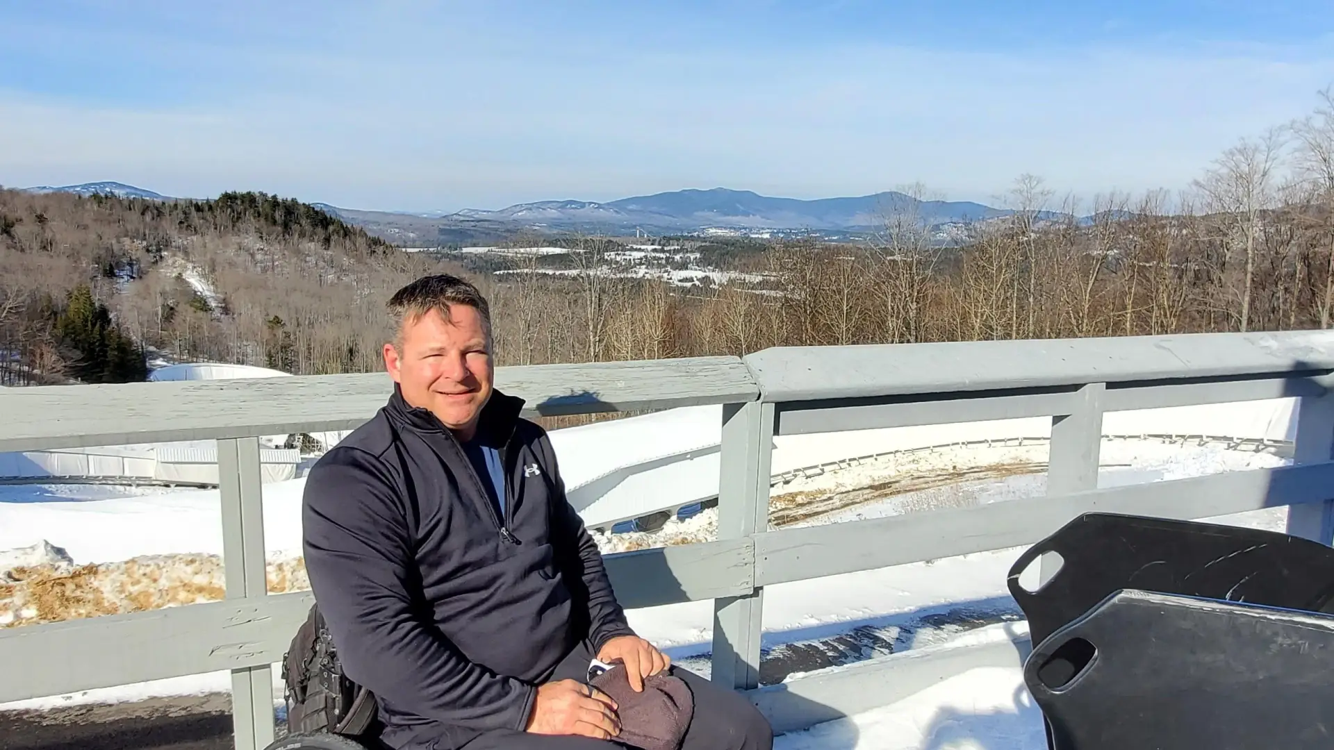 David Christopher in his wheelchair smiling with a wintery Lake Placid behind him. Image courtesy of David Christopher.