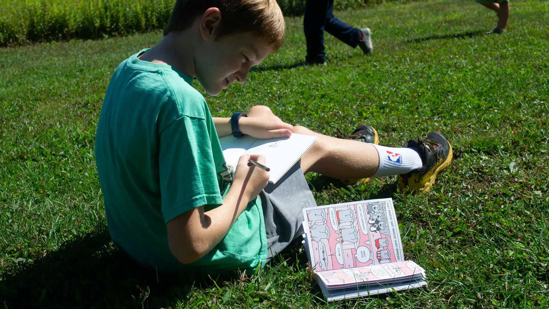 A young boy reads a book on the grass.