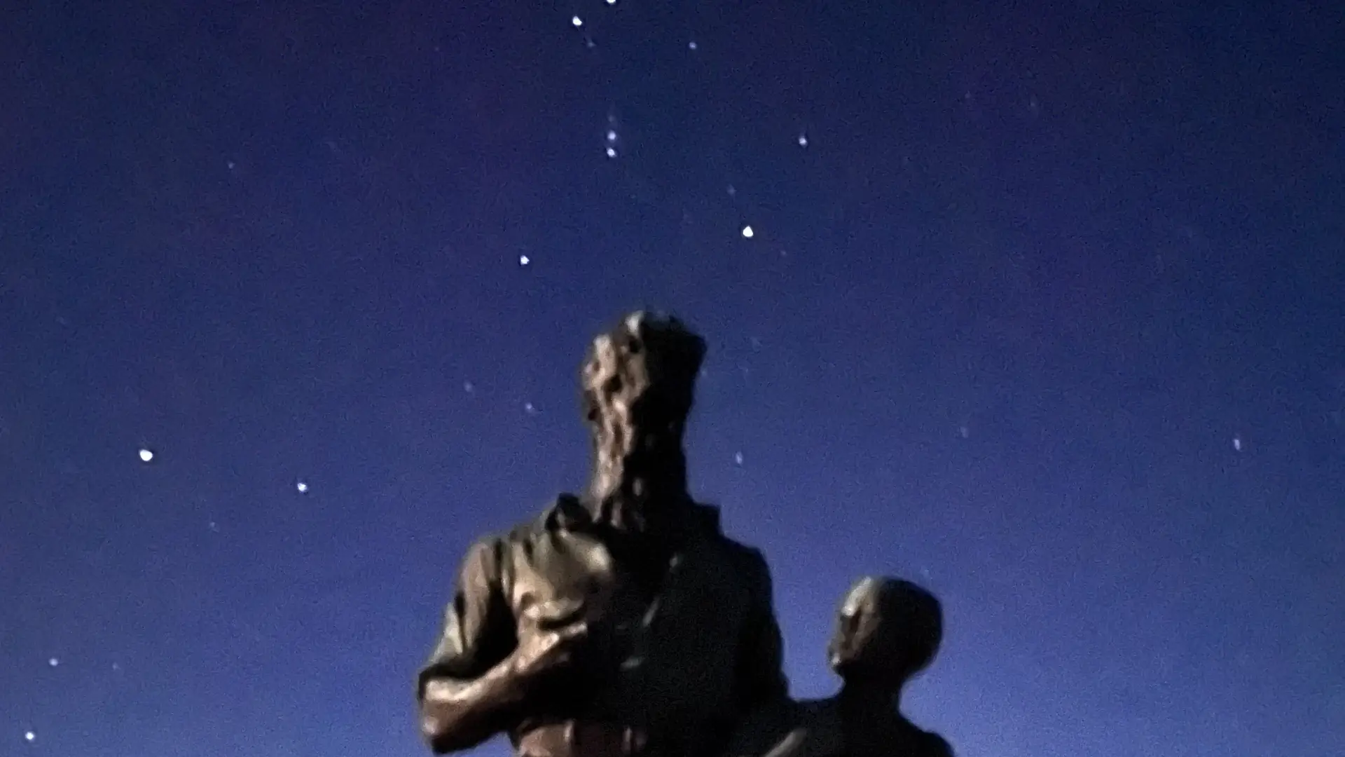 Blurry image of stars in the night sky behind an upshot angle of a John Brown and boy statue