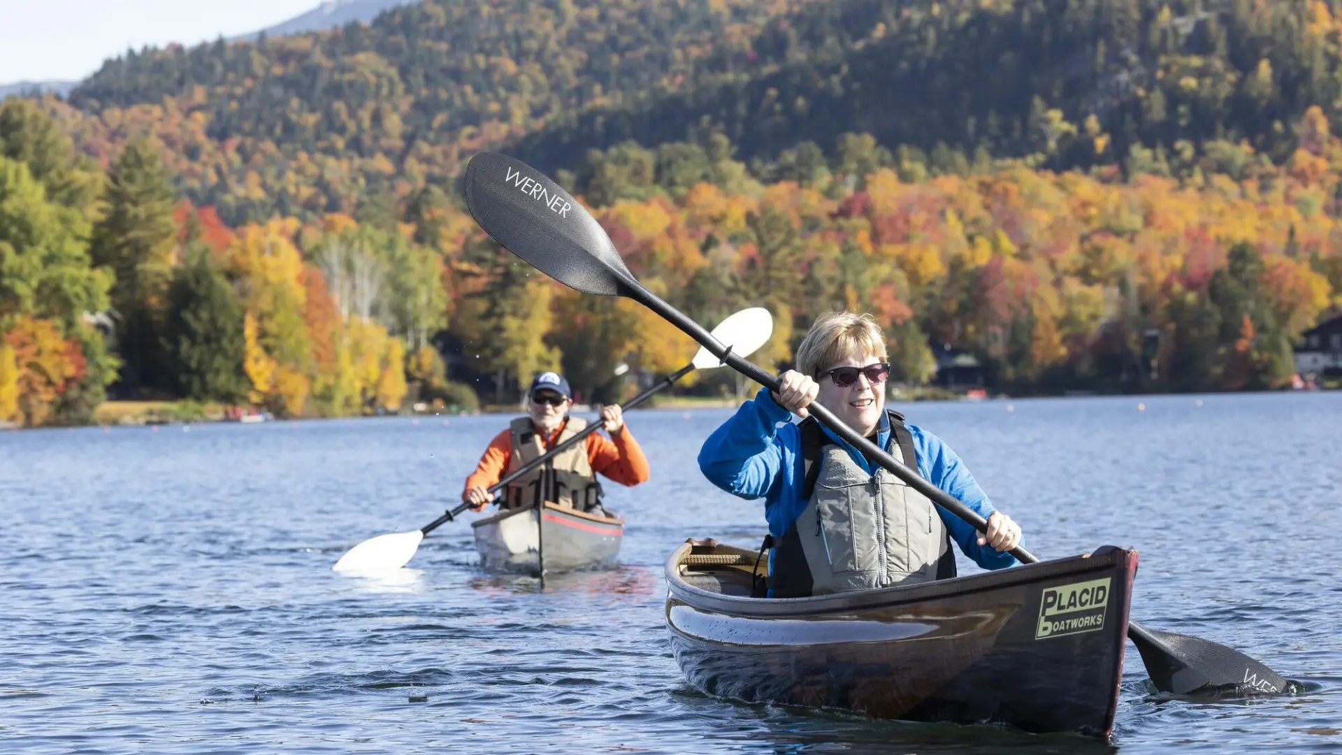 A man and woman paddle in canoes in fall.