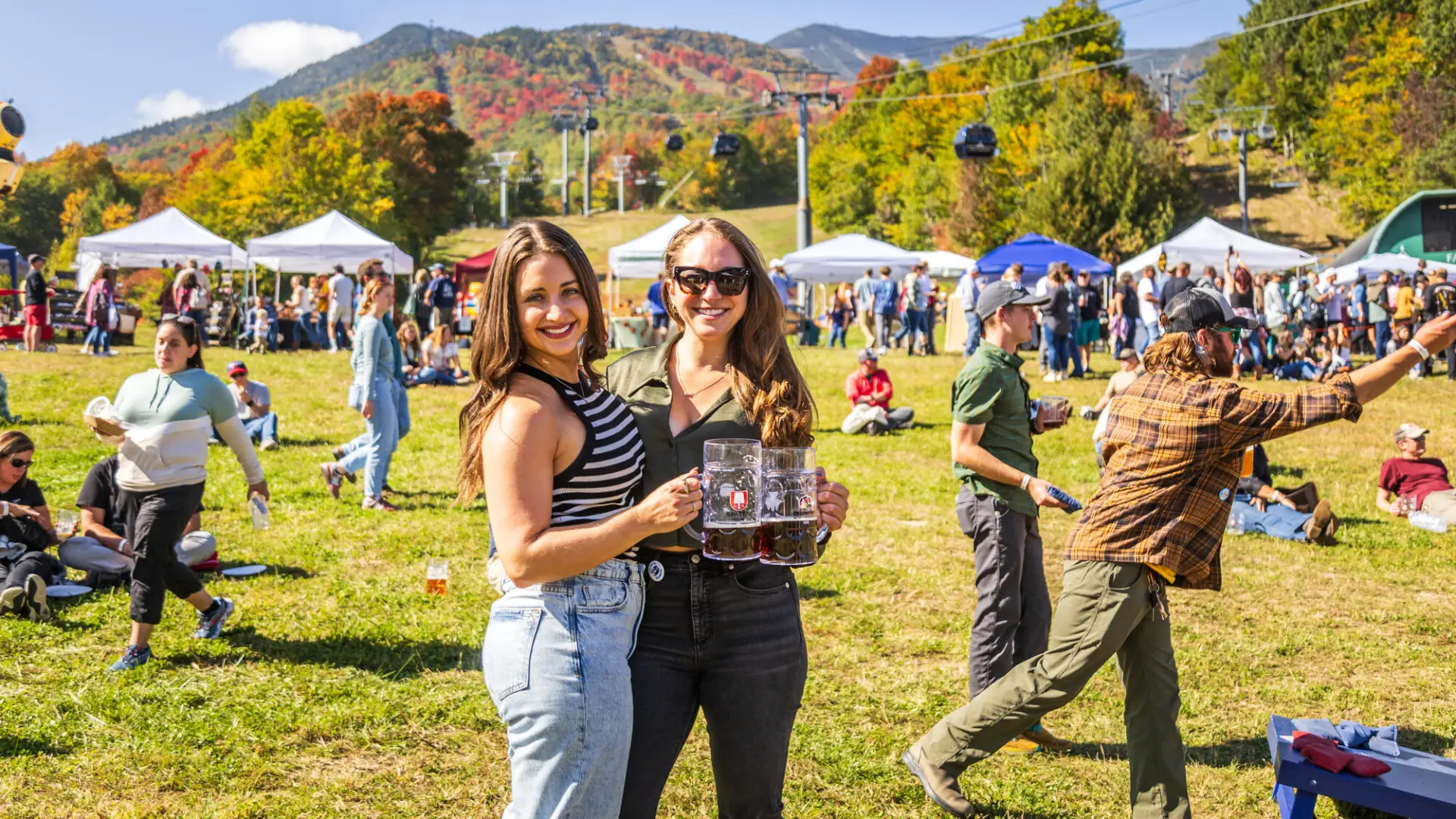 Two women standing with drinks at an outdoor fall event in Lake Placid.