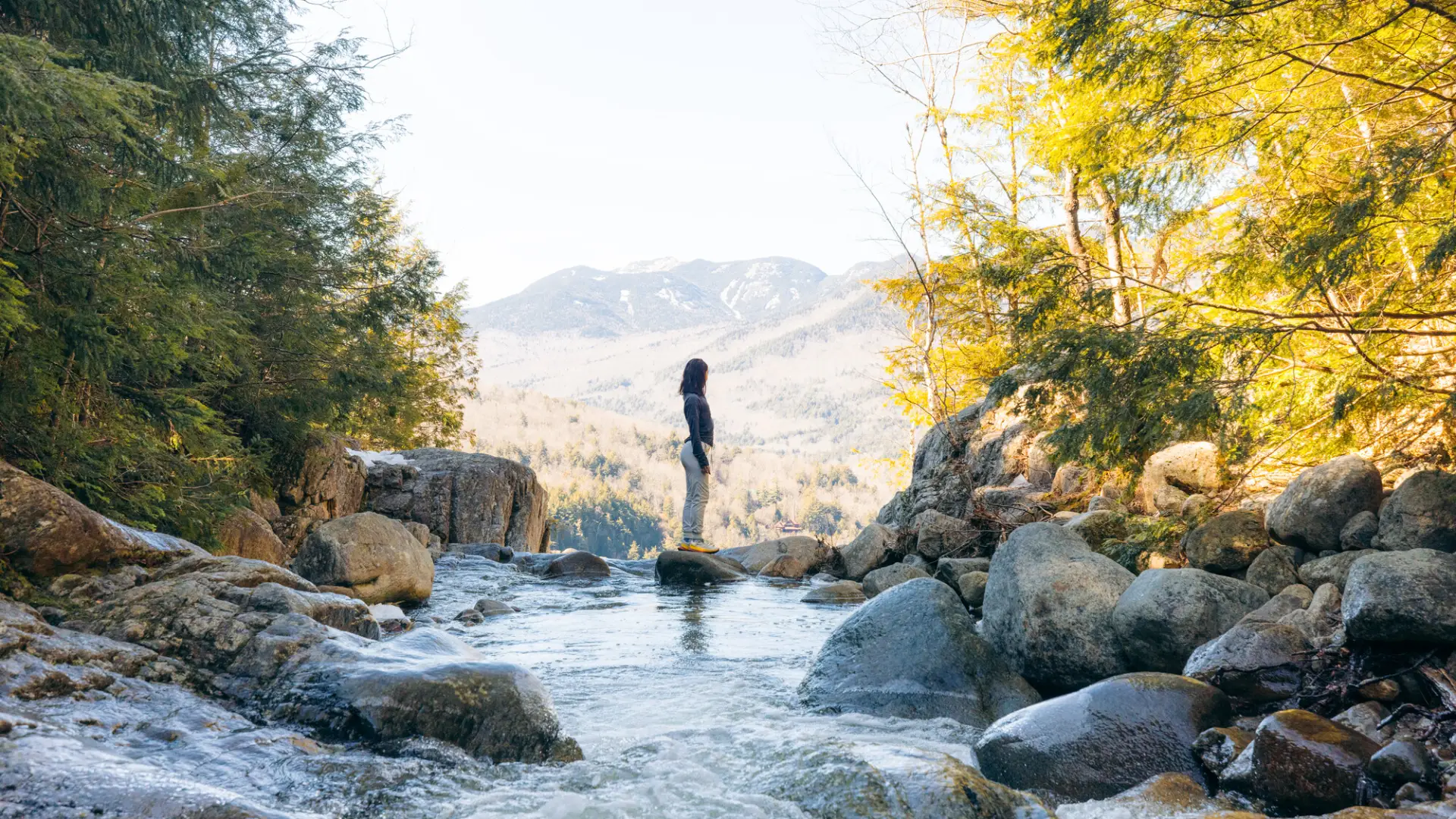 A hiker standing on a rock while crossing over a small river.