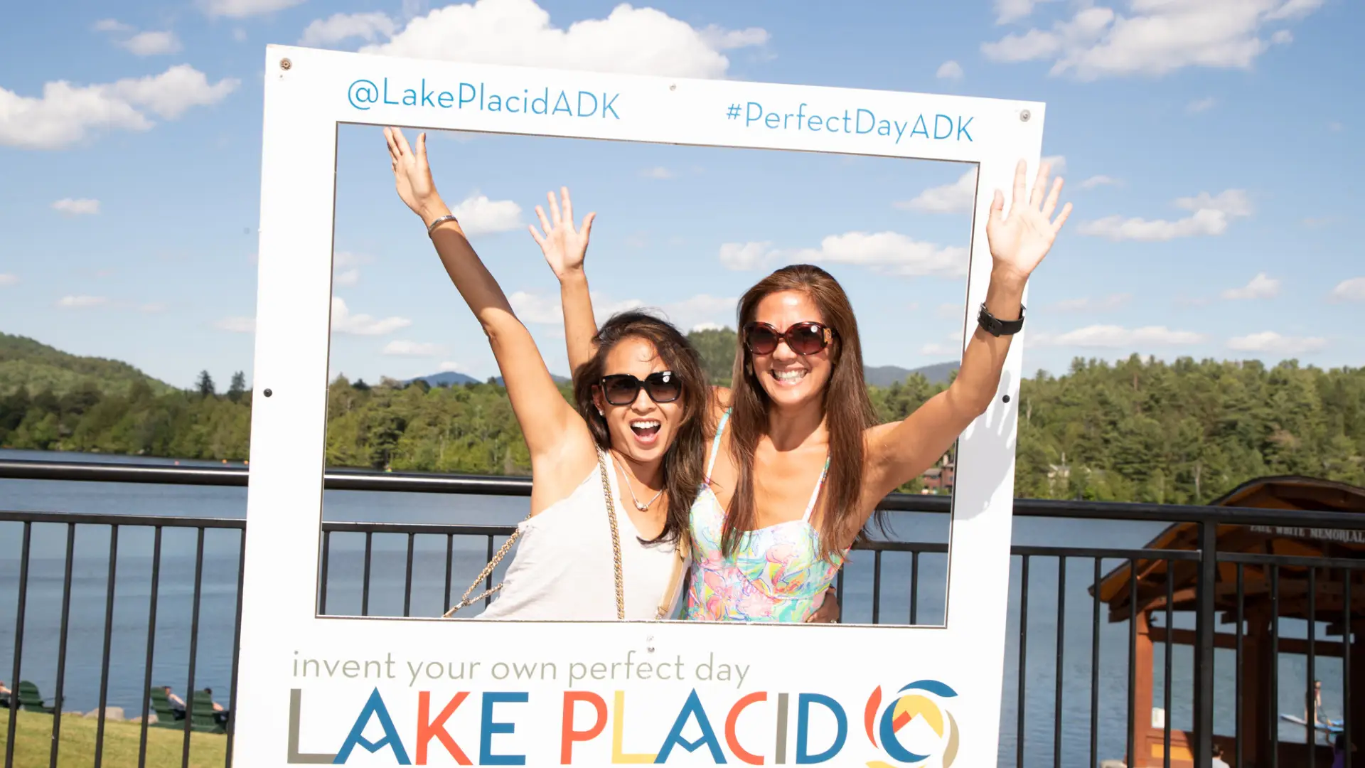 Two women laugh while taking a photo in a Lake Placid frame. 