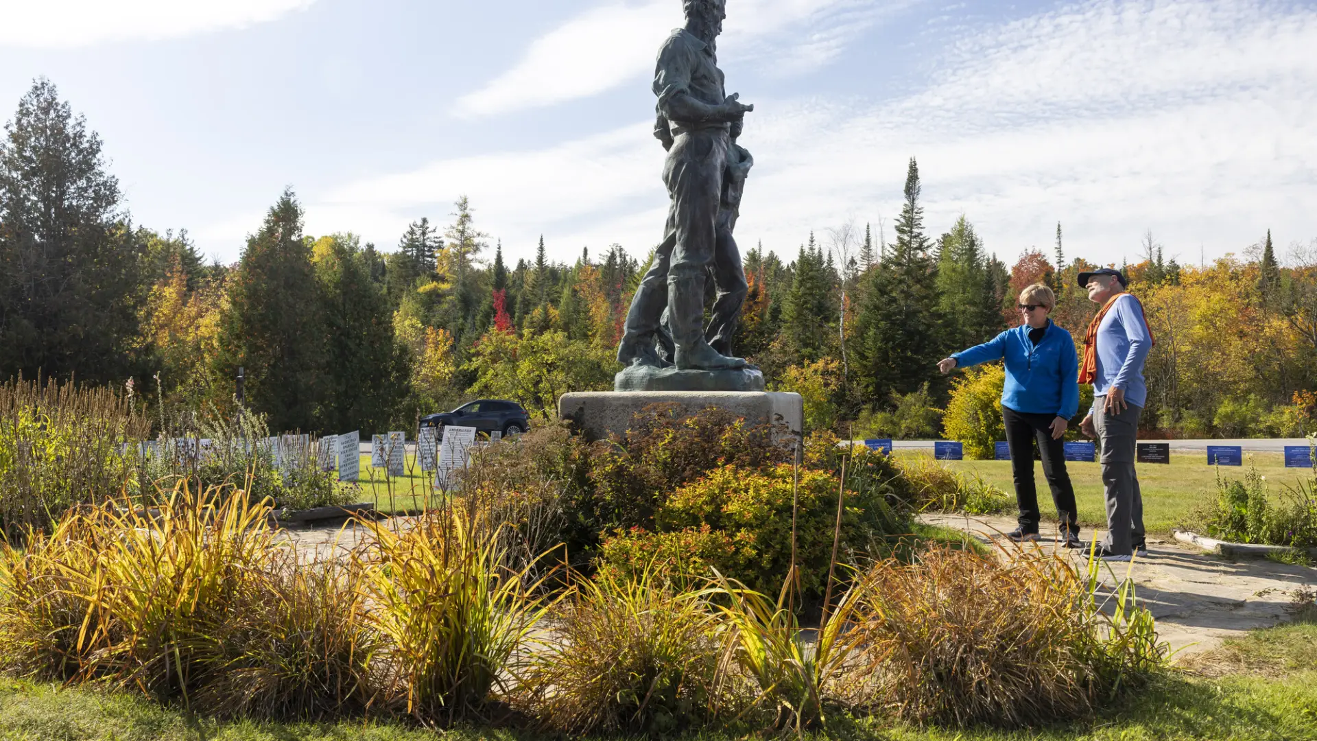 A man and woman look at a statue in a fall field.
