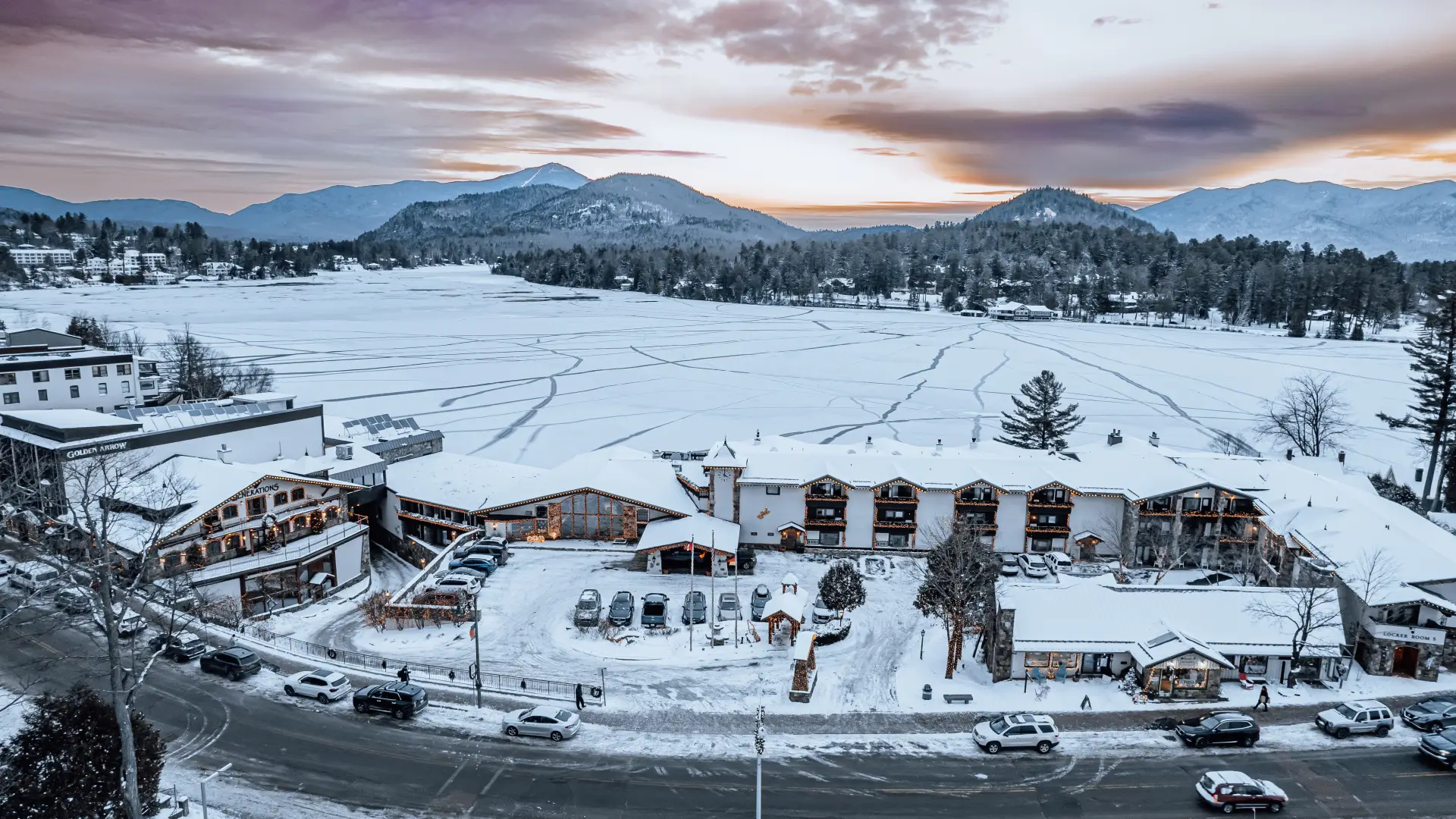 An aerial view of Golden Arrow Lakeside Resort blanketed in snow next to Mirror Lake and the mountains beyond.