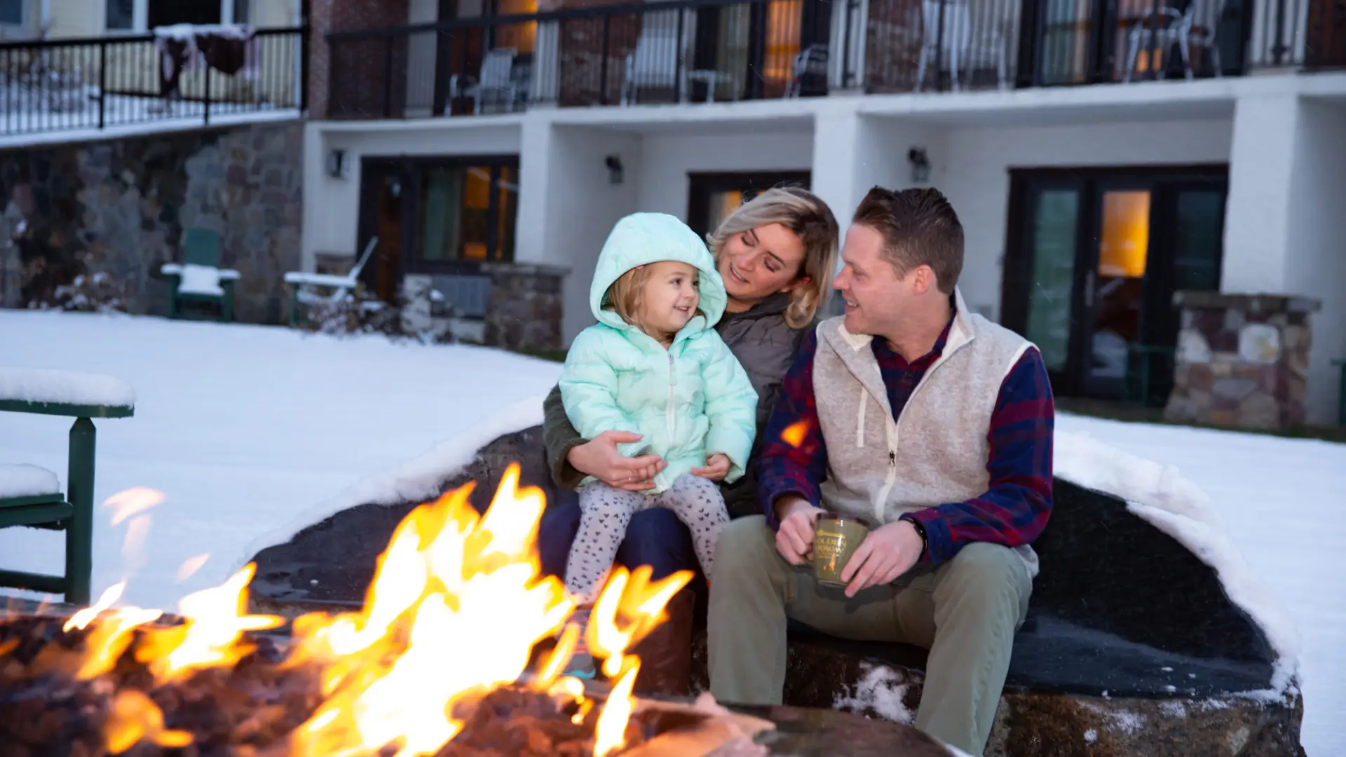 A couple with their child in front of a fire outdoors.
