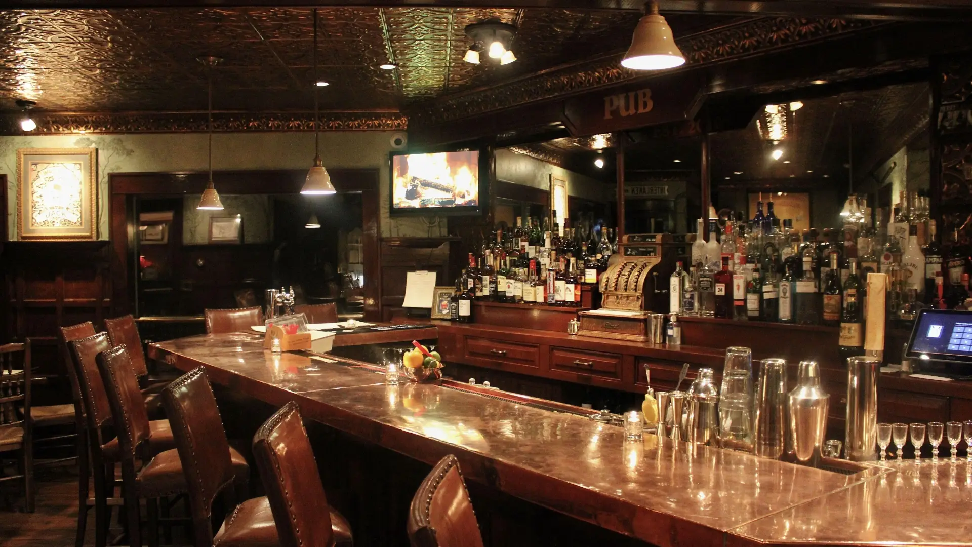 A dark and moody bar with lush leather stools and tin ceiling.