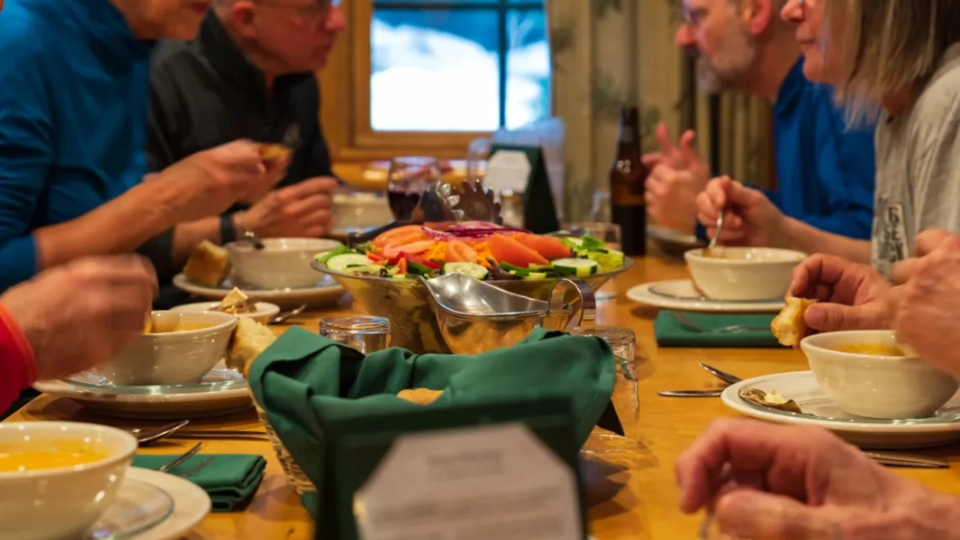 People seated at wooden dining table eating with family-style meal laid out on center of table
