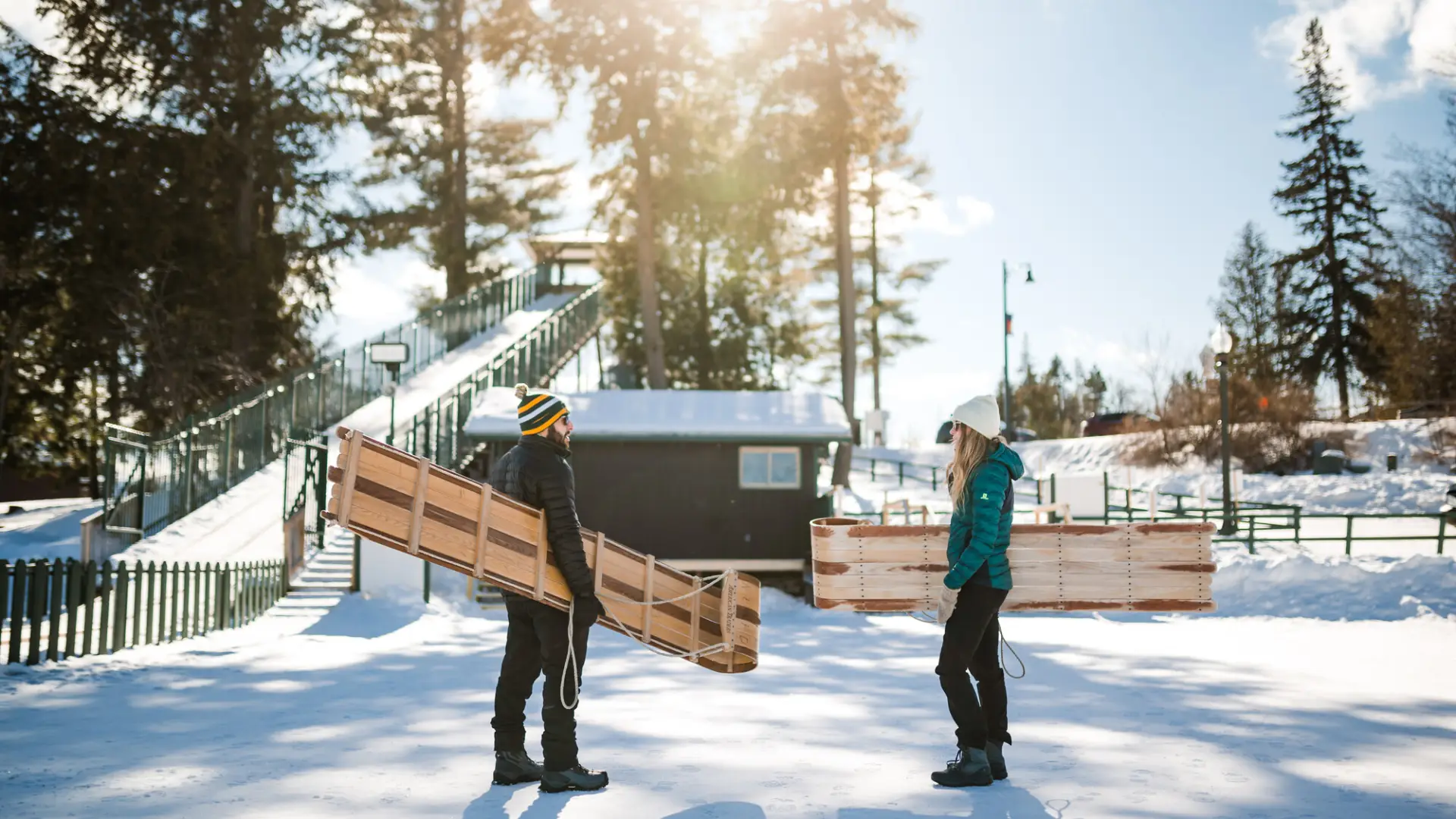 A man and woman chat on the ice while carrying toboggan sleds.