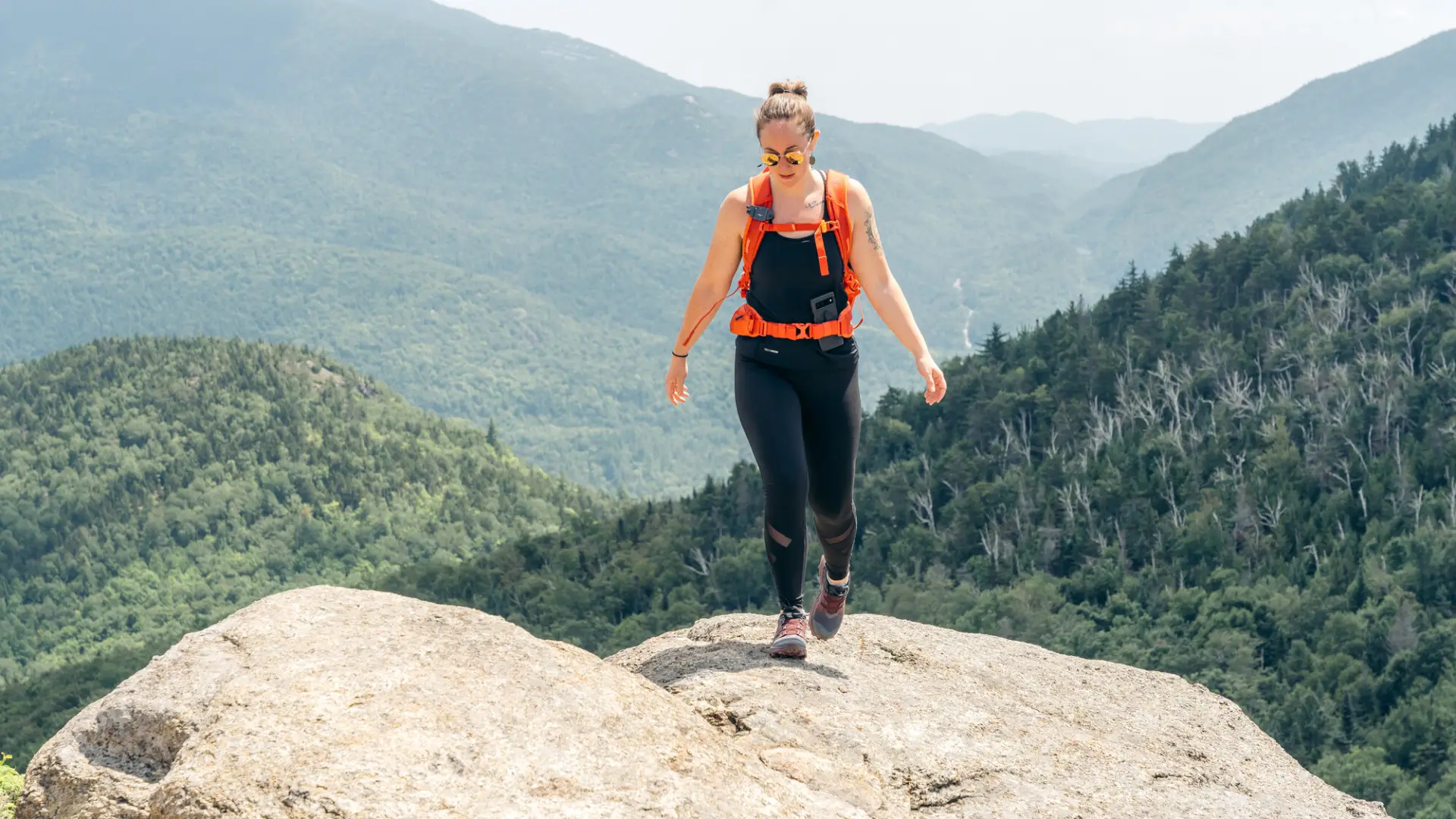 A woman walks on top of a rocky mountain. 