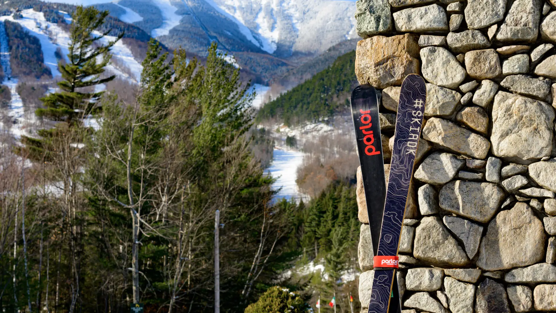 Skis propped against stone wall with Whiteface trails visible in background