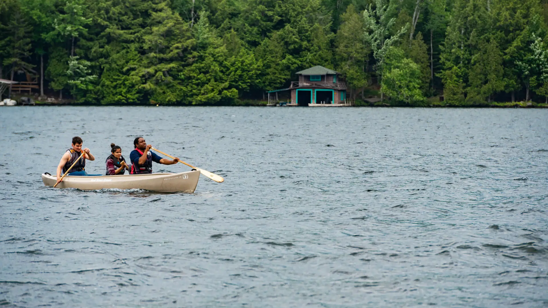 A man paddles with two passengers in a canoe.