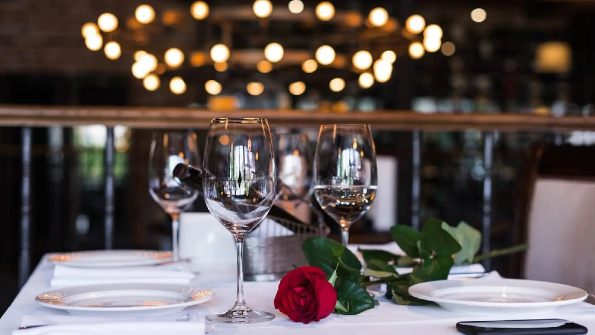 Wine glasses and a rose sit on a table with white tablecloth.