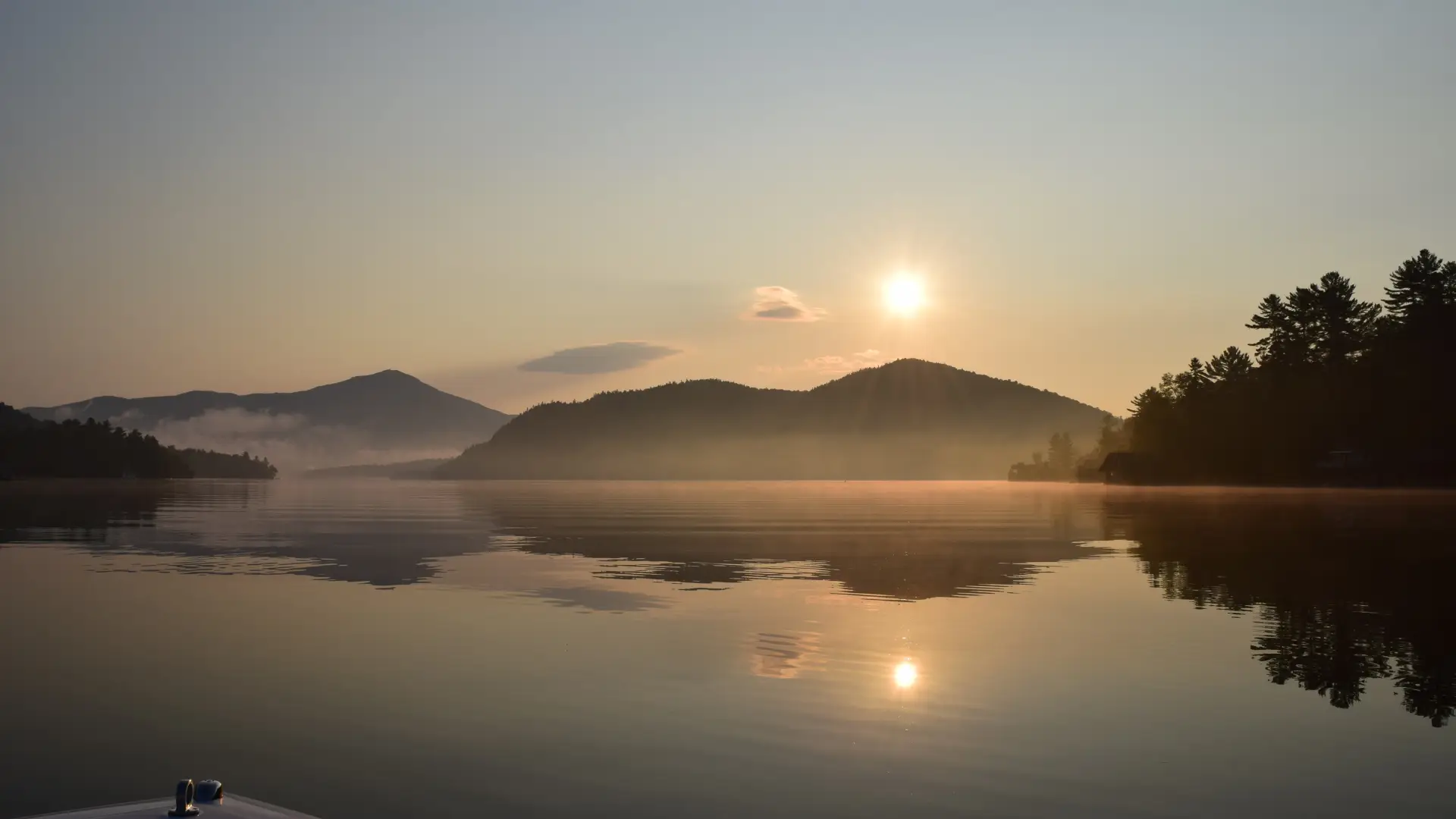 A ride on the boat on a smooth, misty lake with the mountains in the distance and the sun setting