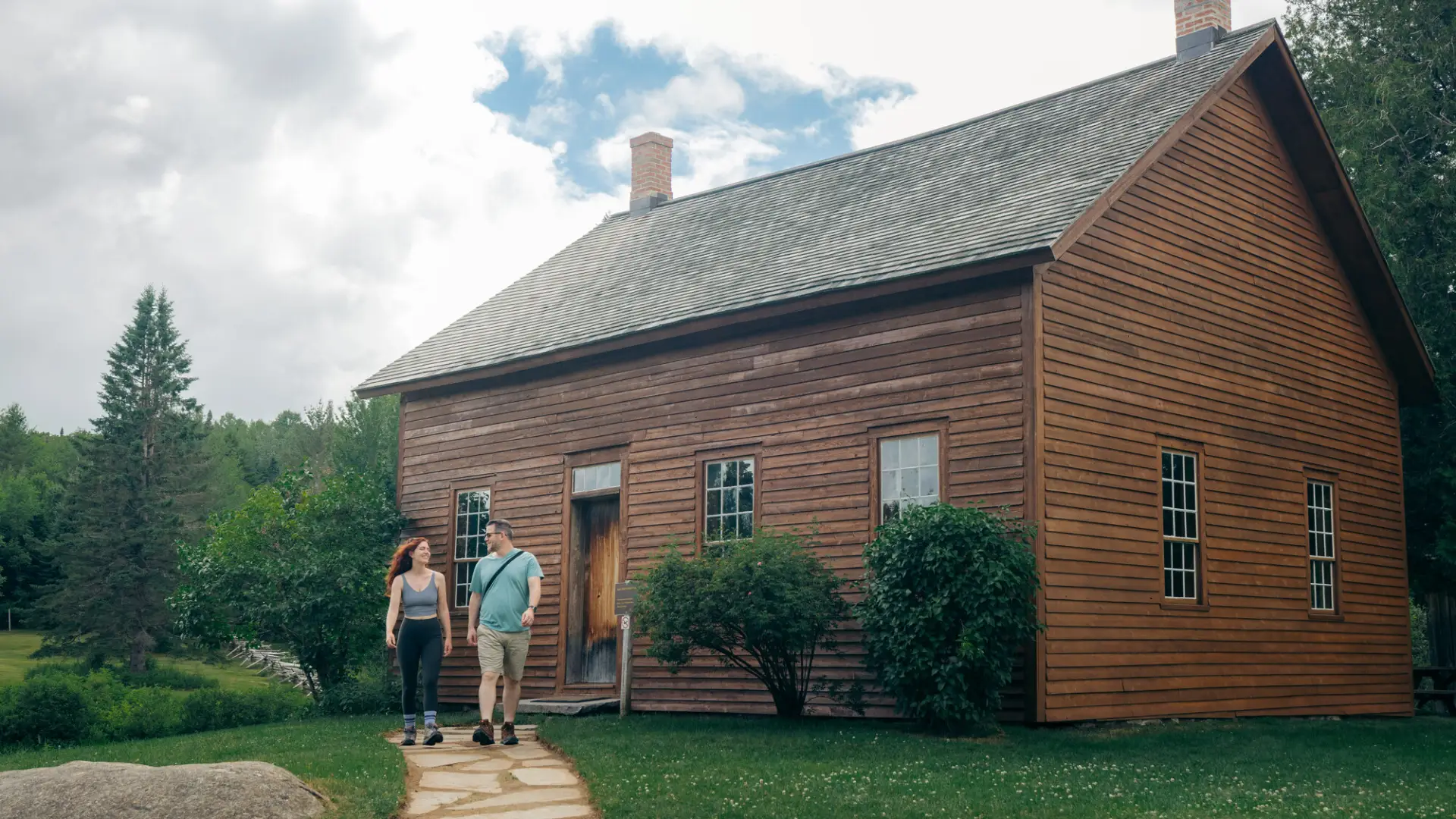 Couple in summer clothing walk out of barn at John Brown Farm State Historic Site in summer