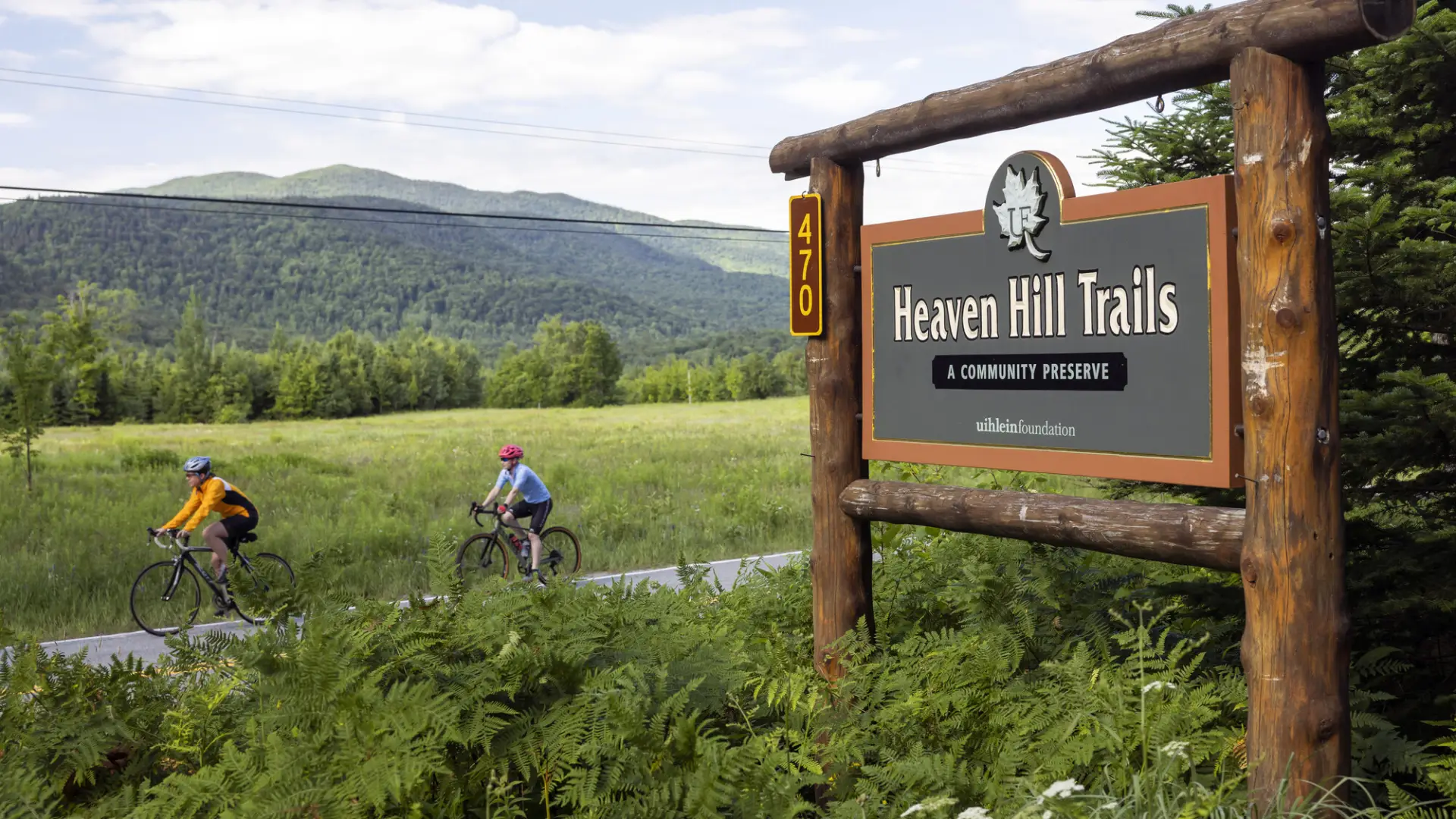 Two people on bikes ride past the Heaven Hill Trails sign.