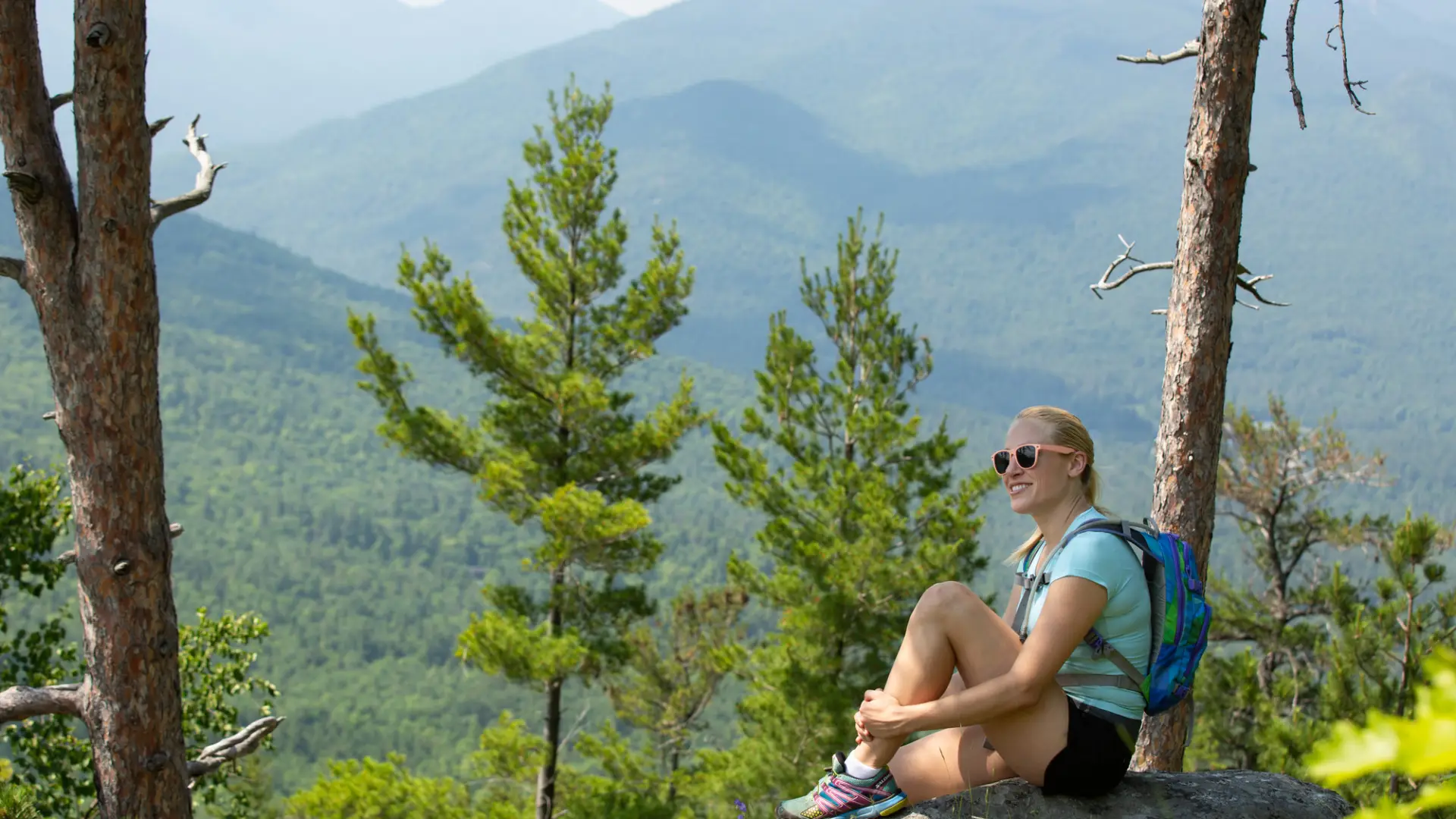 A woman sitting on a rock on top of a mountain overlooking the peaks in the distance.