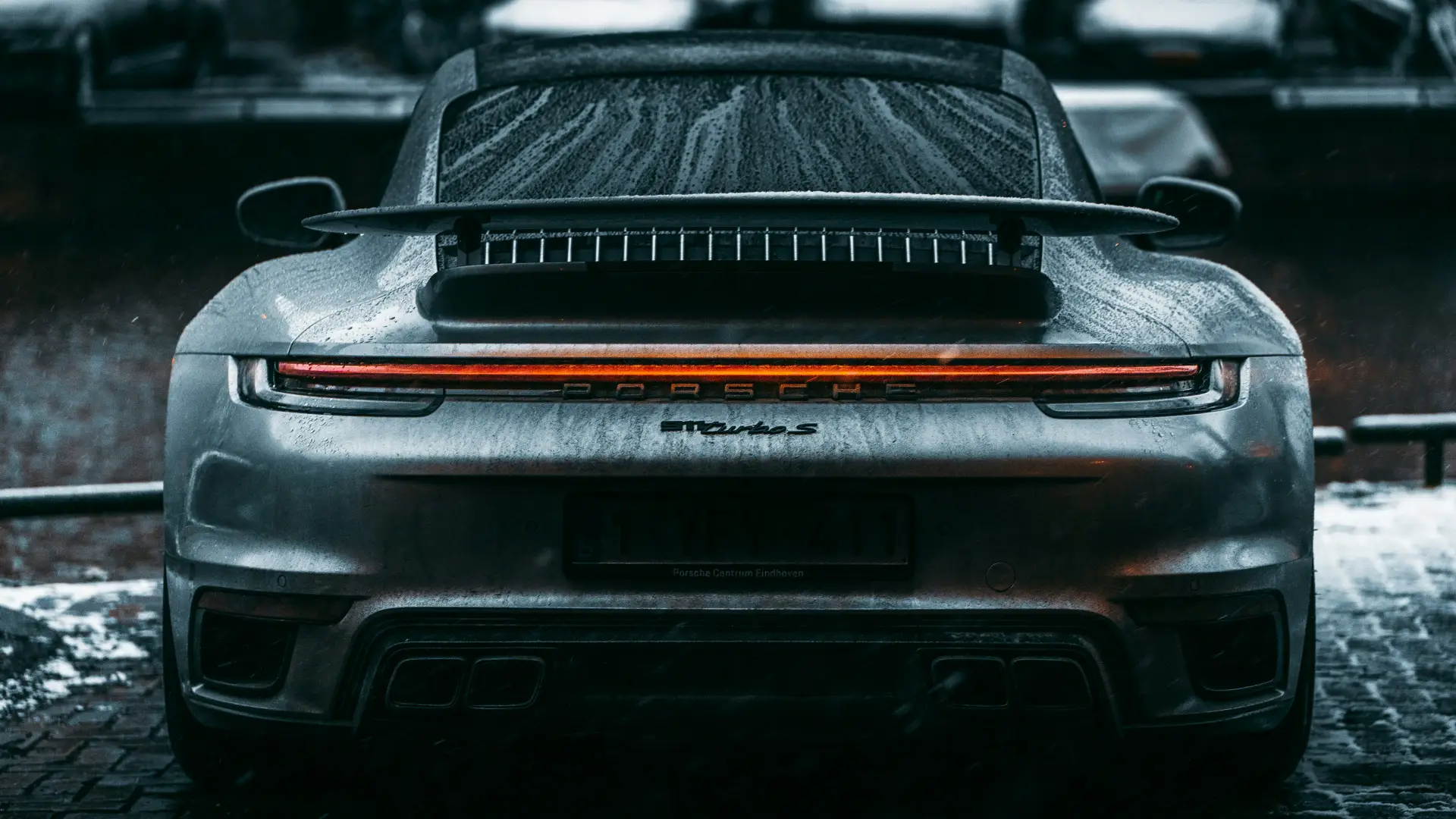 Stock image of the rear of a dark grey Porche sports car covered in water droplets interior space
