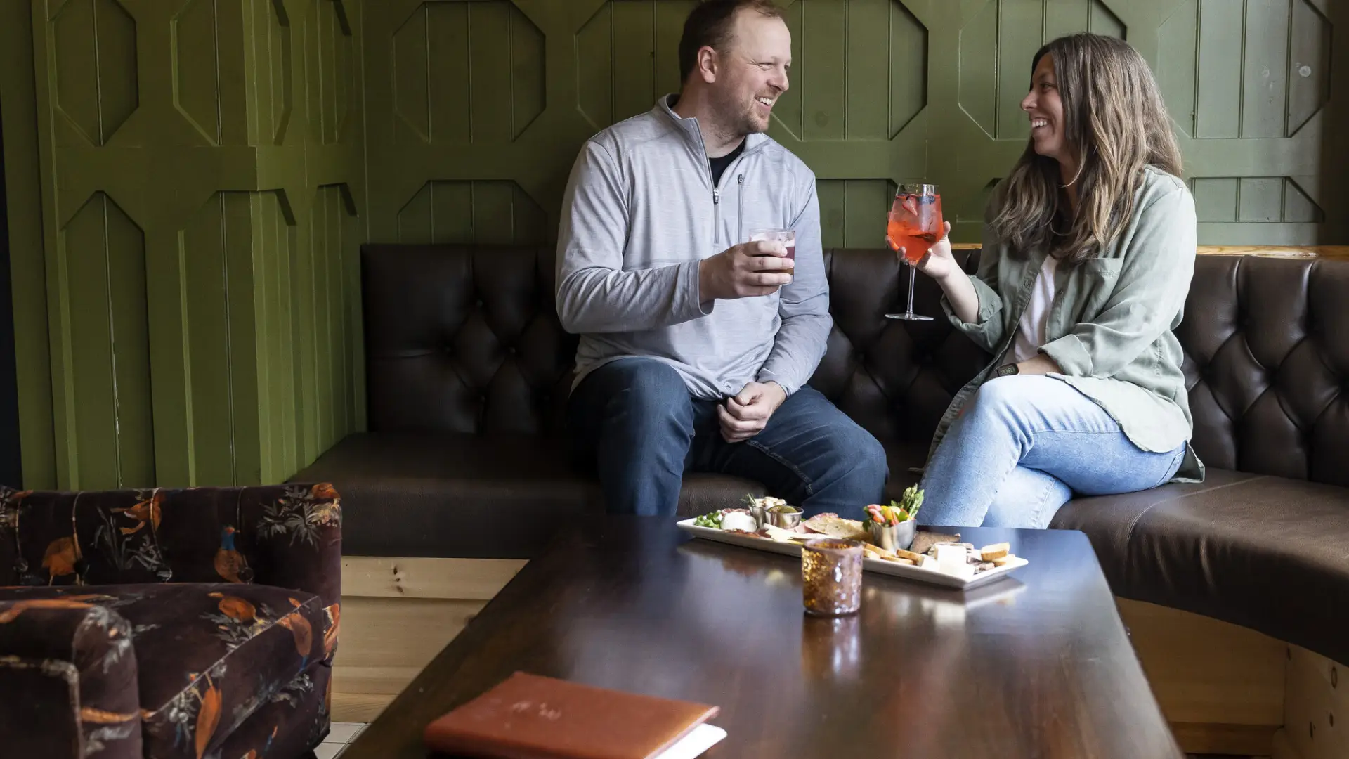 Couple sits on bench seat with cocktails and food on table