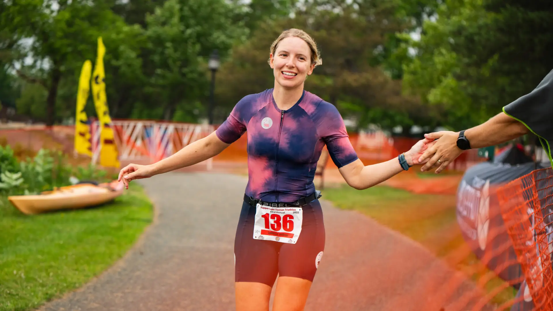 A smiling triathlete reaches out for a high-five while running toward the finish line of the Tupper Lake Tinman Triathlon.