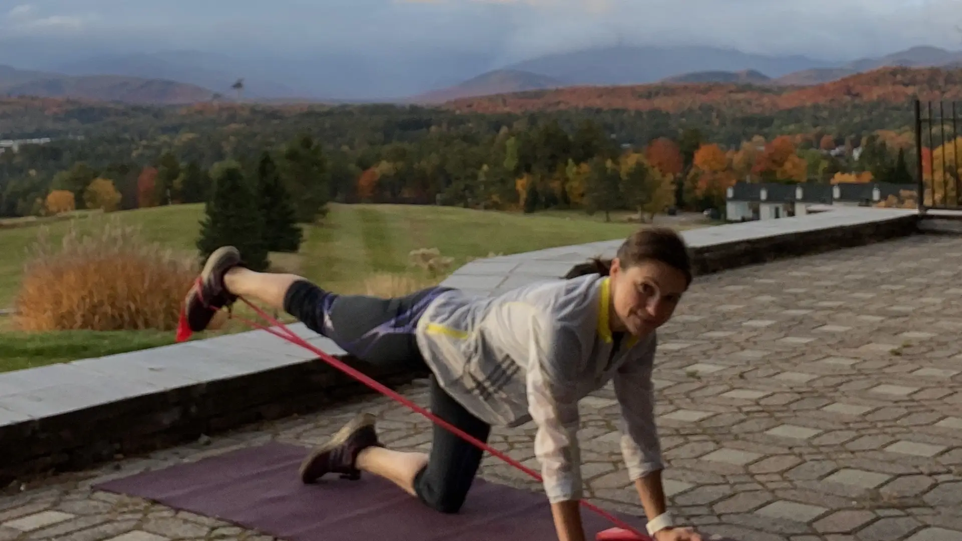 Woman doing a leg extension exercise with a resistance band outdoors with scenic mountain view in the background.