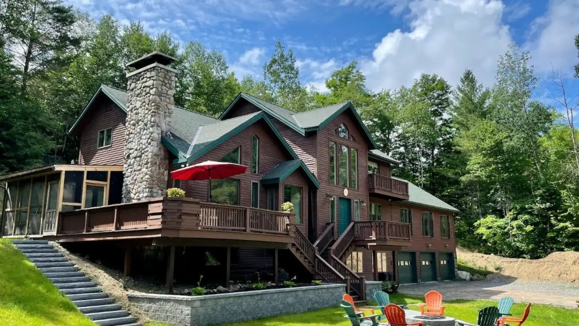A large log home with huge windows, multiple decks and balconies, screen porch and stacked stone chimney.