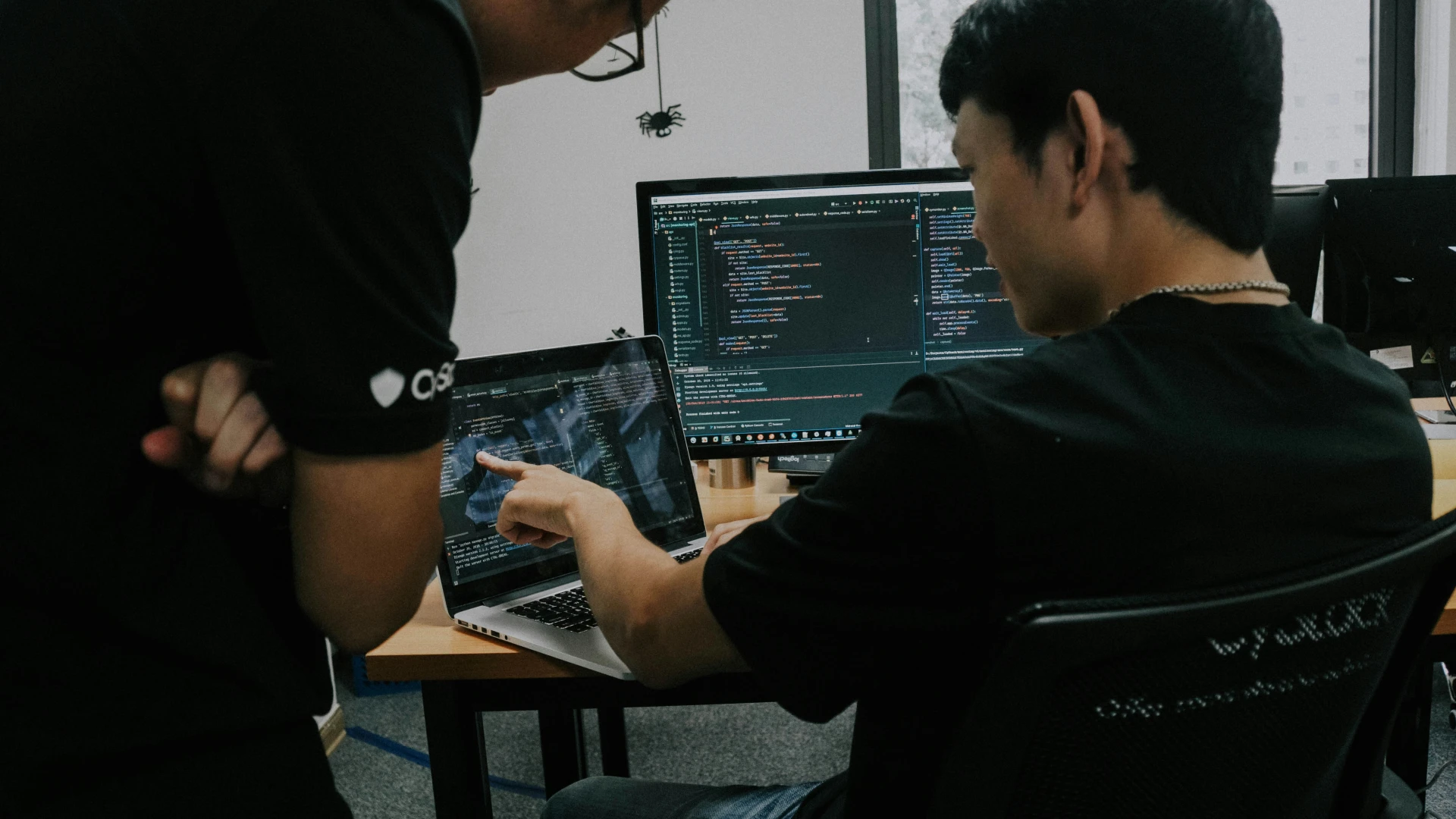 Person working on laptop with additional monitor pointing to screen while a second person leans over their shoulder