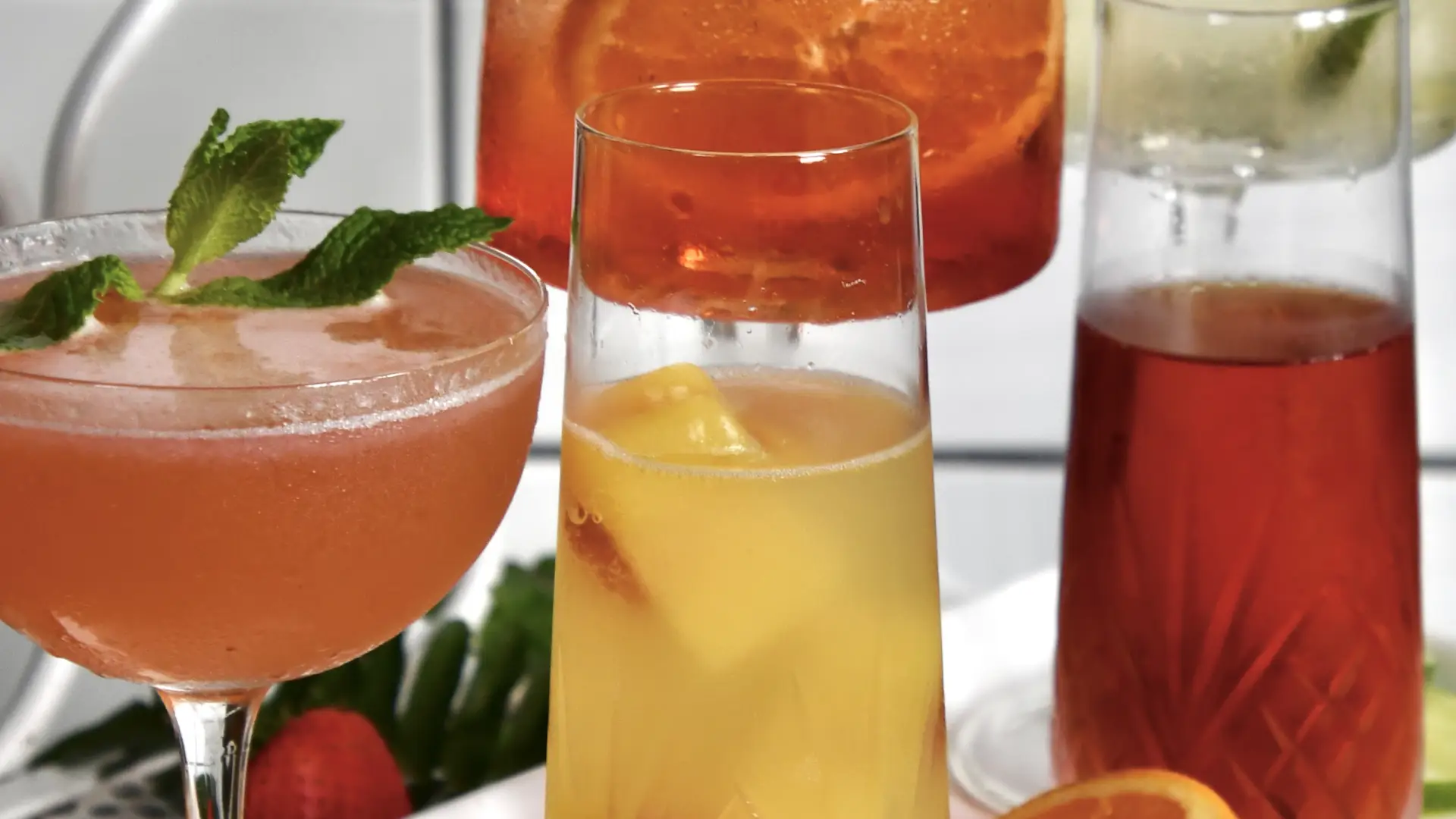 Tray of colorful cocktails in various glass types on a white plate with citrus garnishes