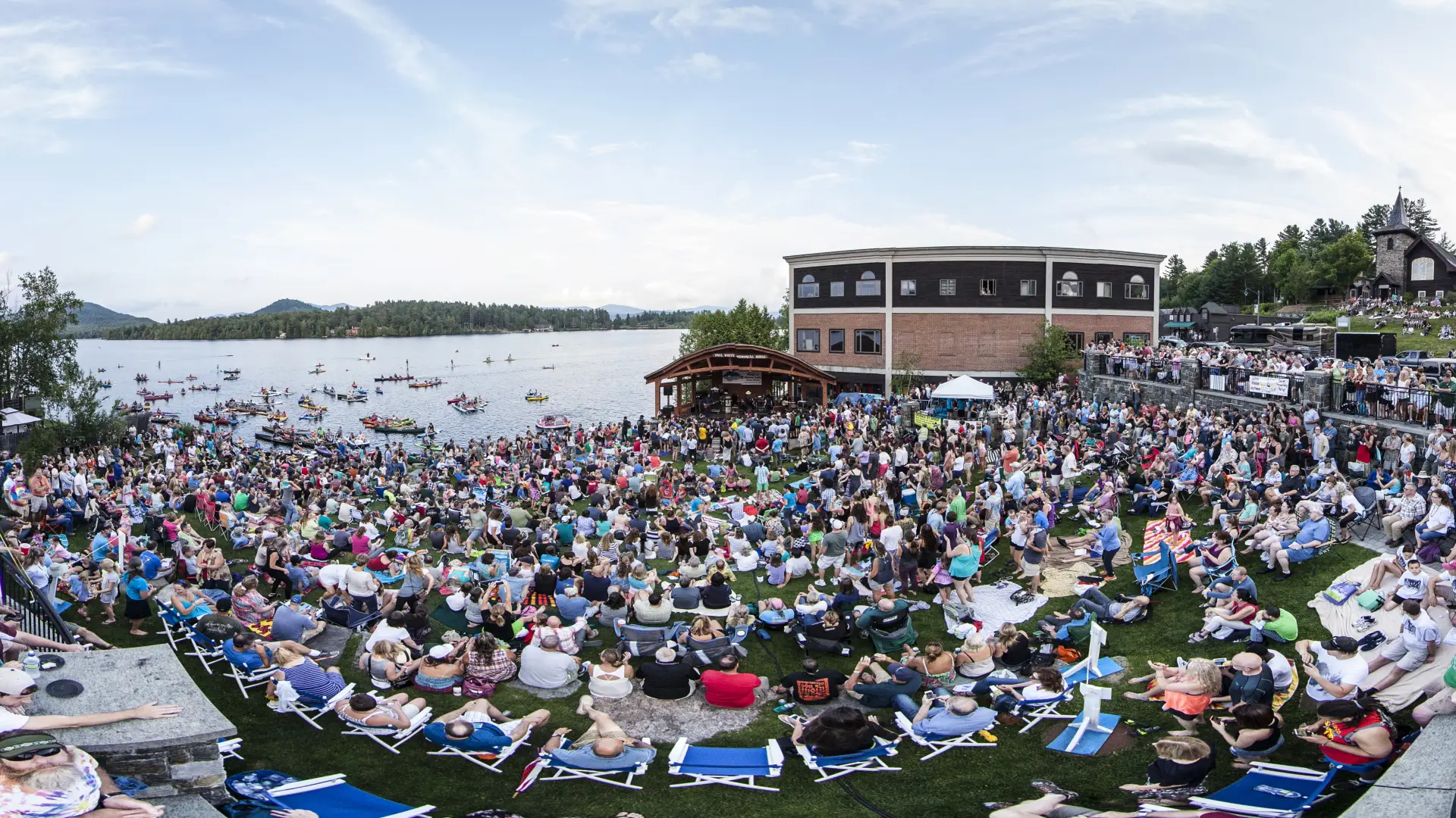 A large group of people gathered at a bandshell by the water