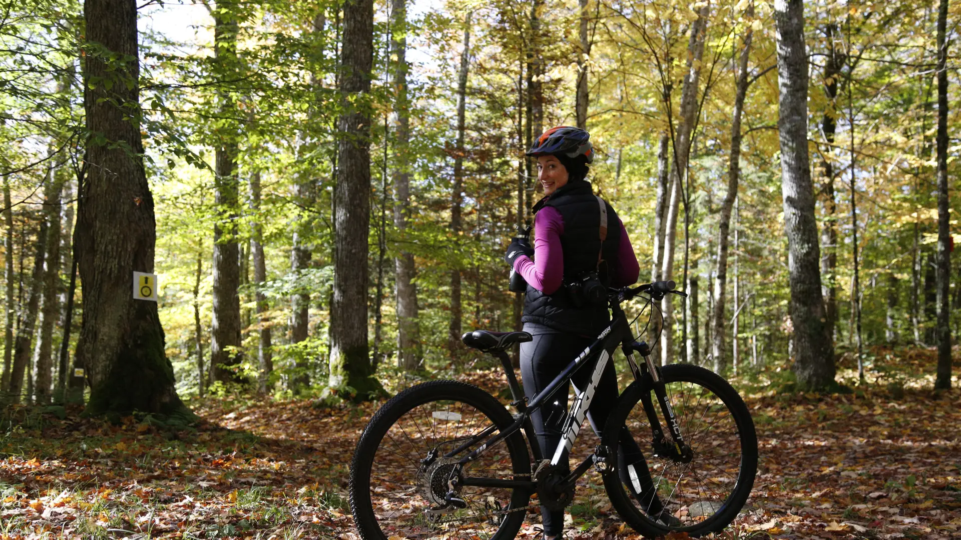"Female smiling at the camera with a Lake Placid mountain bike rental surrounded by fallen leaves