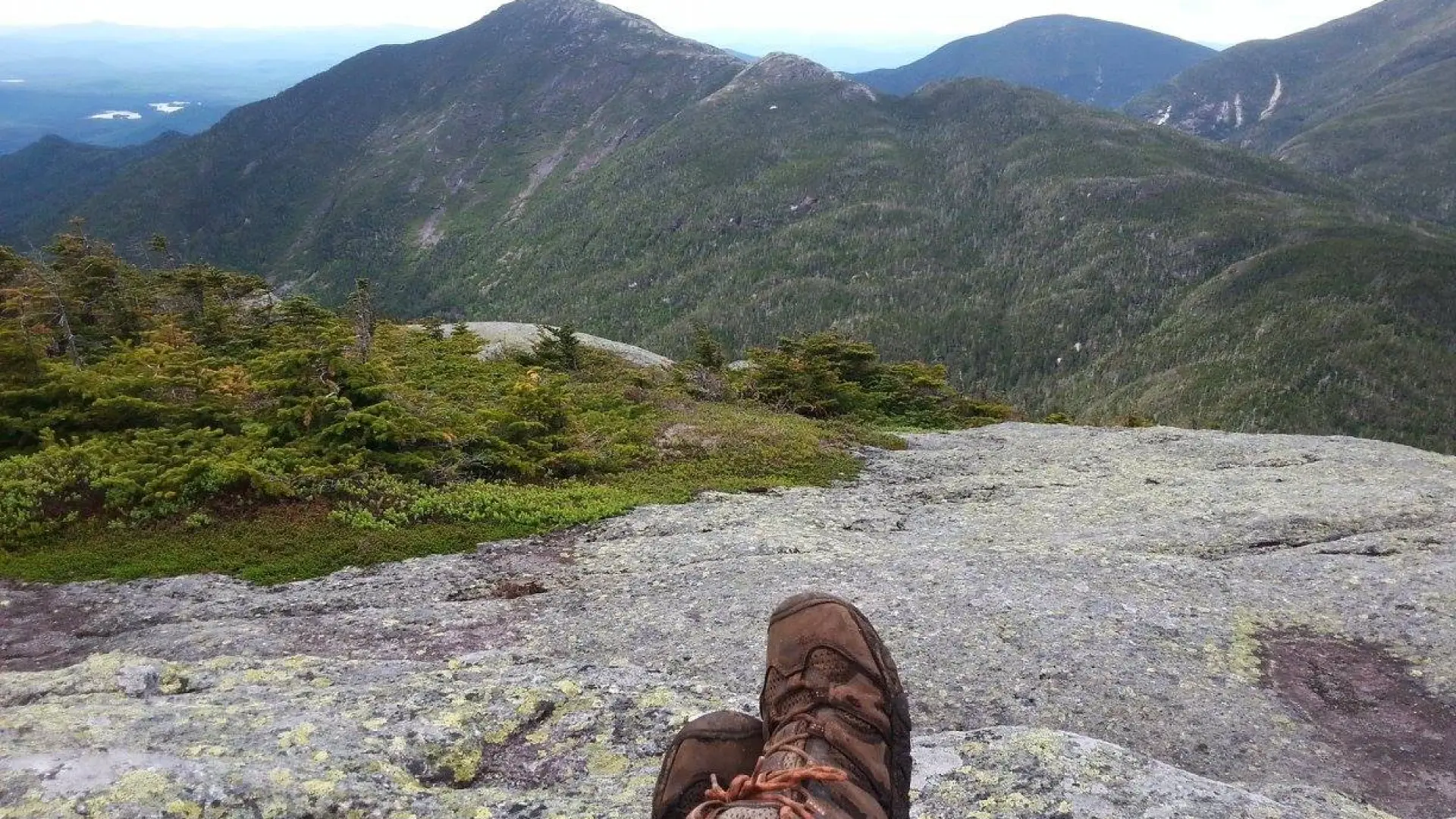 A hiker sits with legs outstretched on the rocky summit of a High Peak.