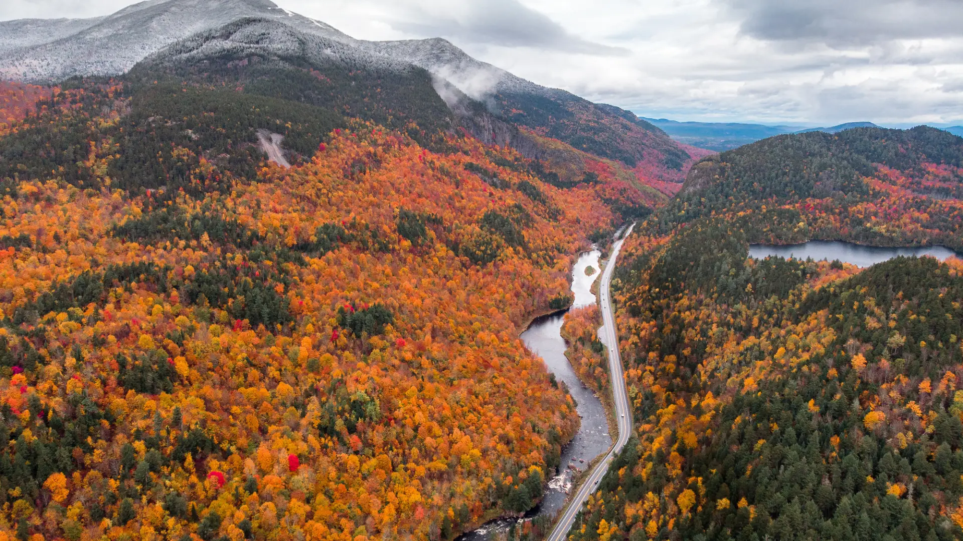 An aerial view of a snow-touched mountain and fall colored trees