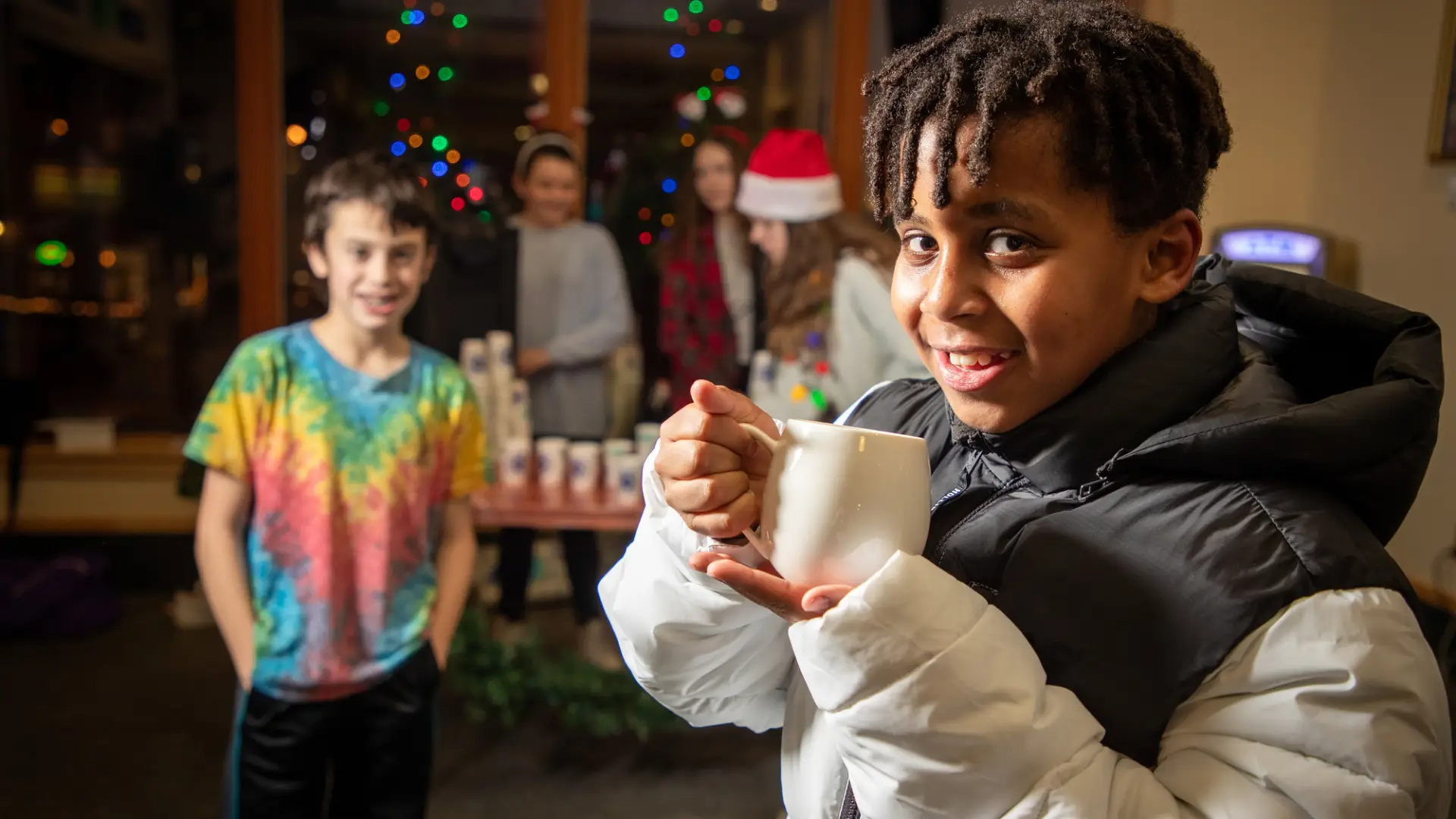 A child sips a hot cocoa with his friend behind him. 