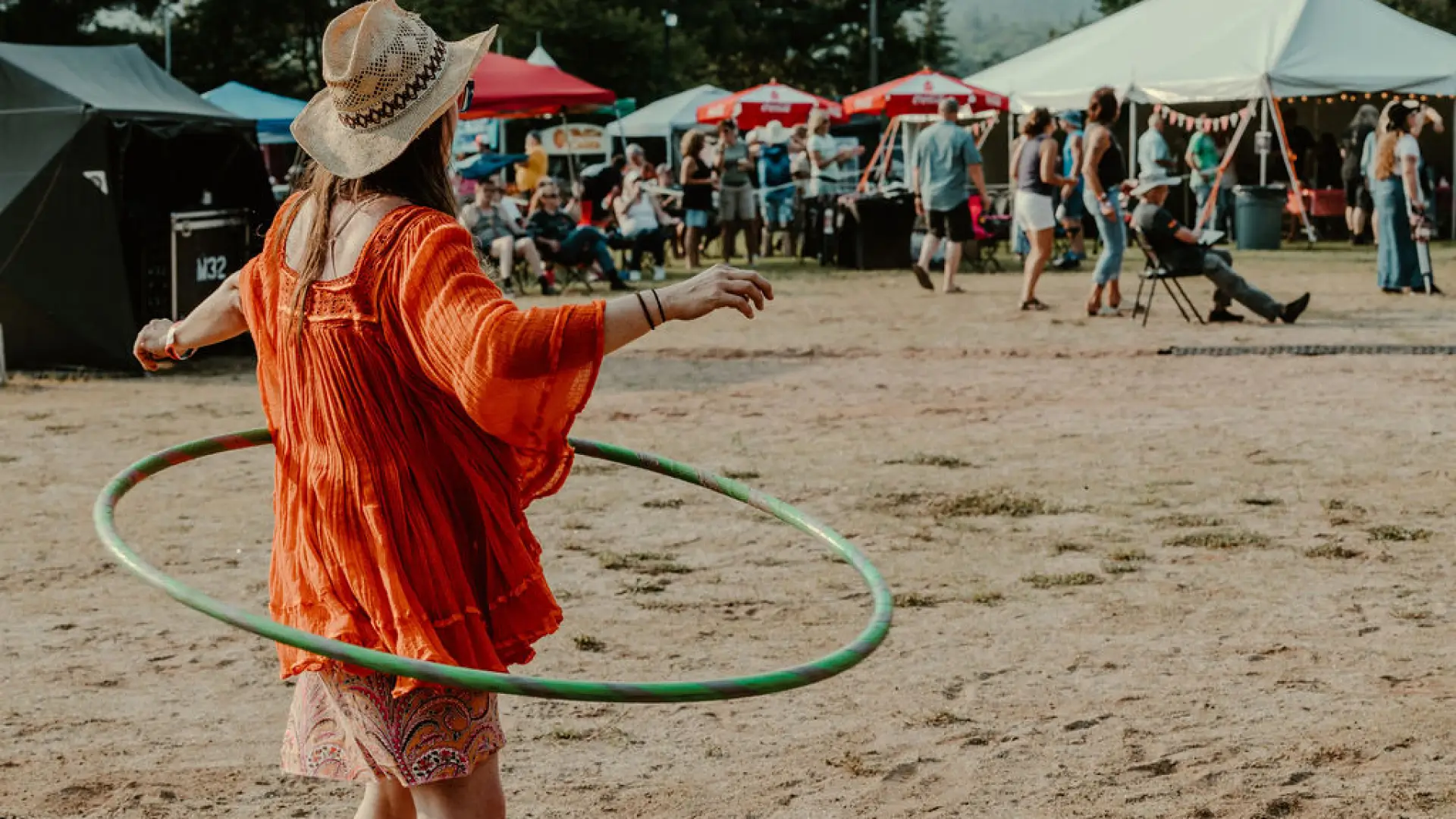 Woman in red dress and straw hat hula hoops in front of smallfestival crowd