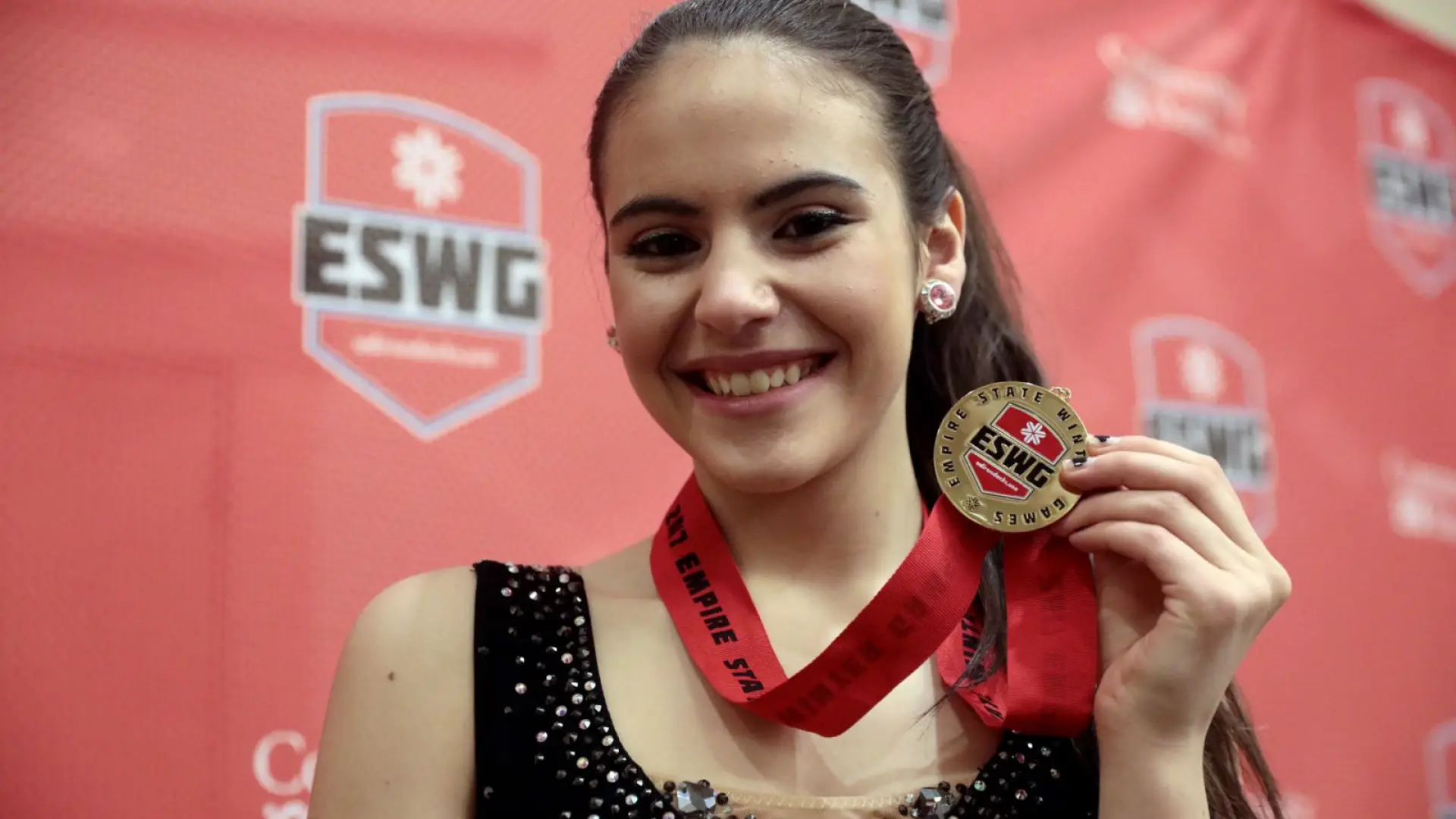 A teenage figure skater smiles and holds up her Empire State Winter Games medal.
