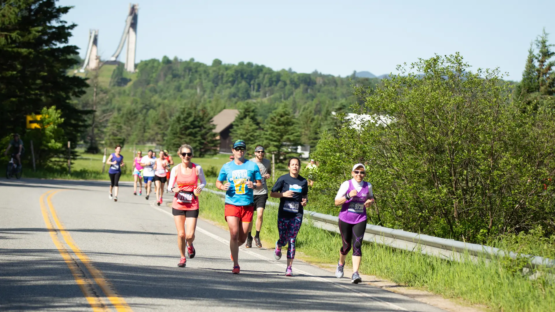 Runners run along a road with the ski jumps in the background
