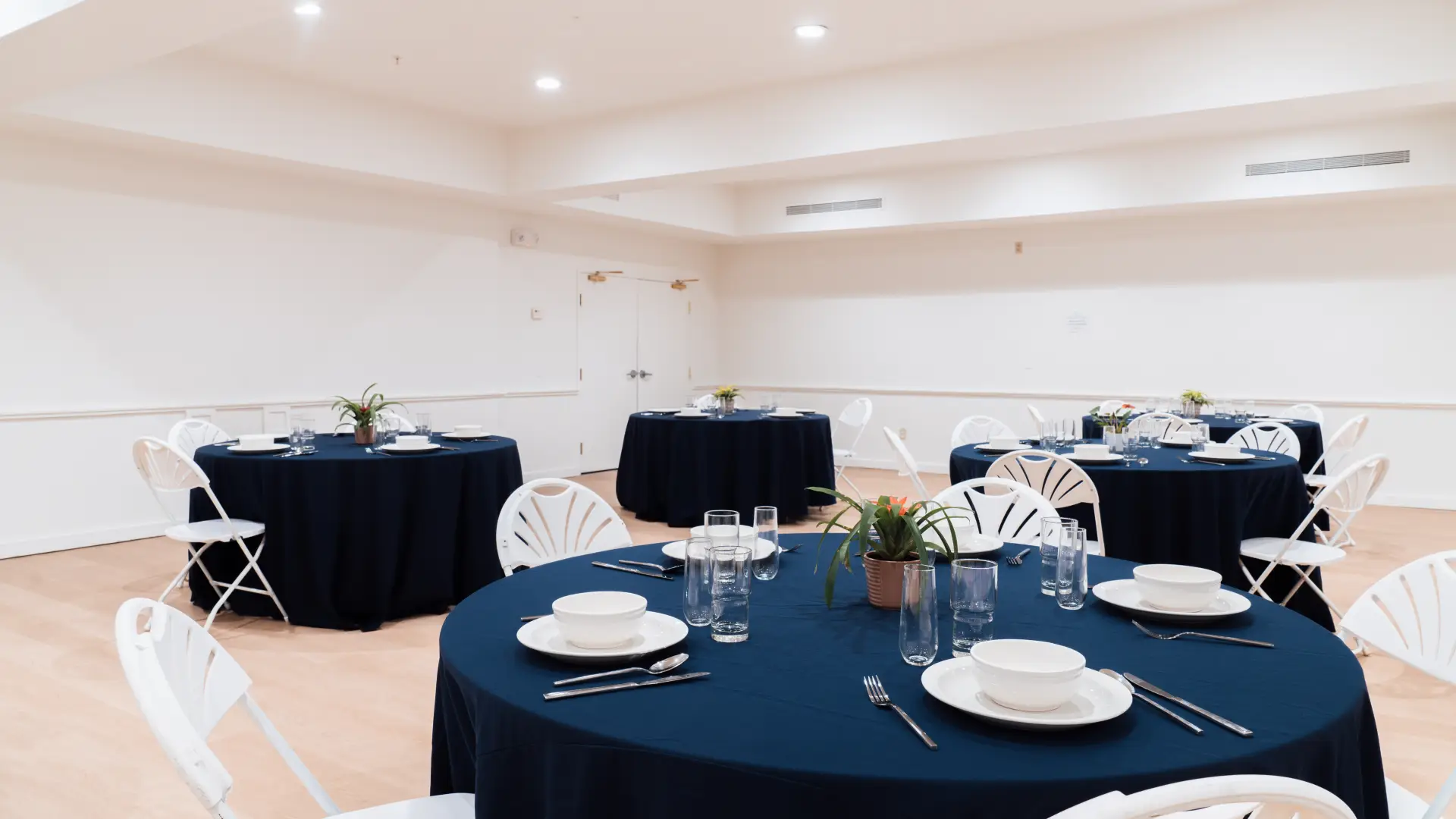 A bright and open space with round tables with deep blue cloths.