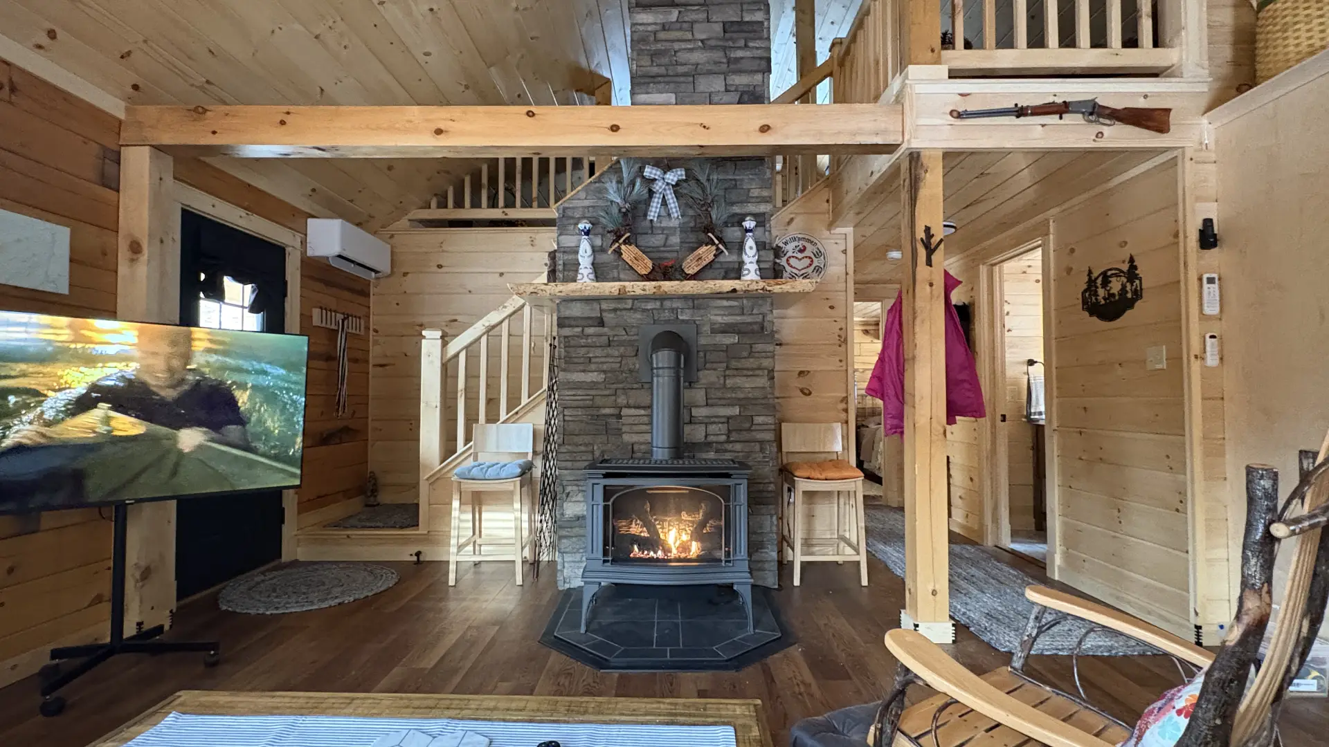 The living space with central stacked stone fireplace and wood stove with stairs to the loft behind.