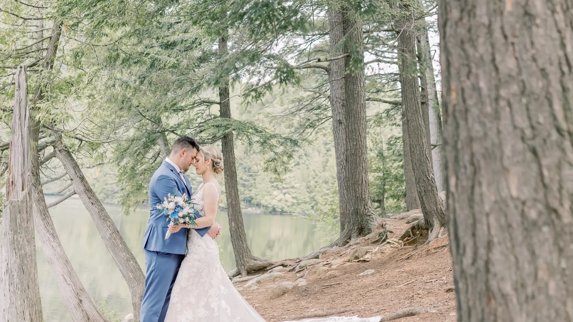 Bride and groom embrace surrounded by cedars next to a tranquil pond