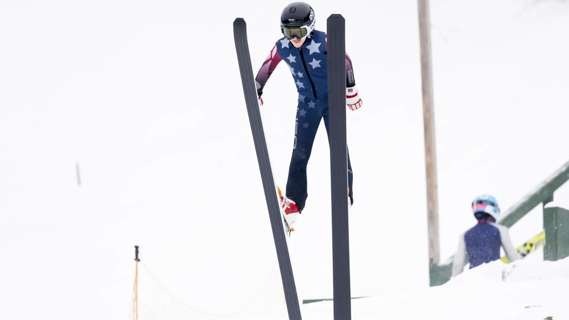 A ski jumper taking flight before a snowy sky.